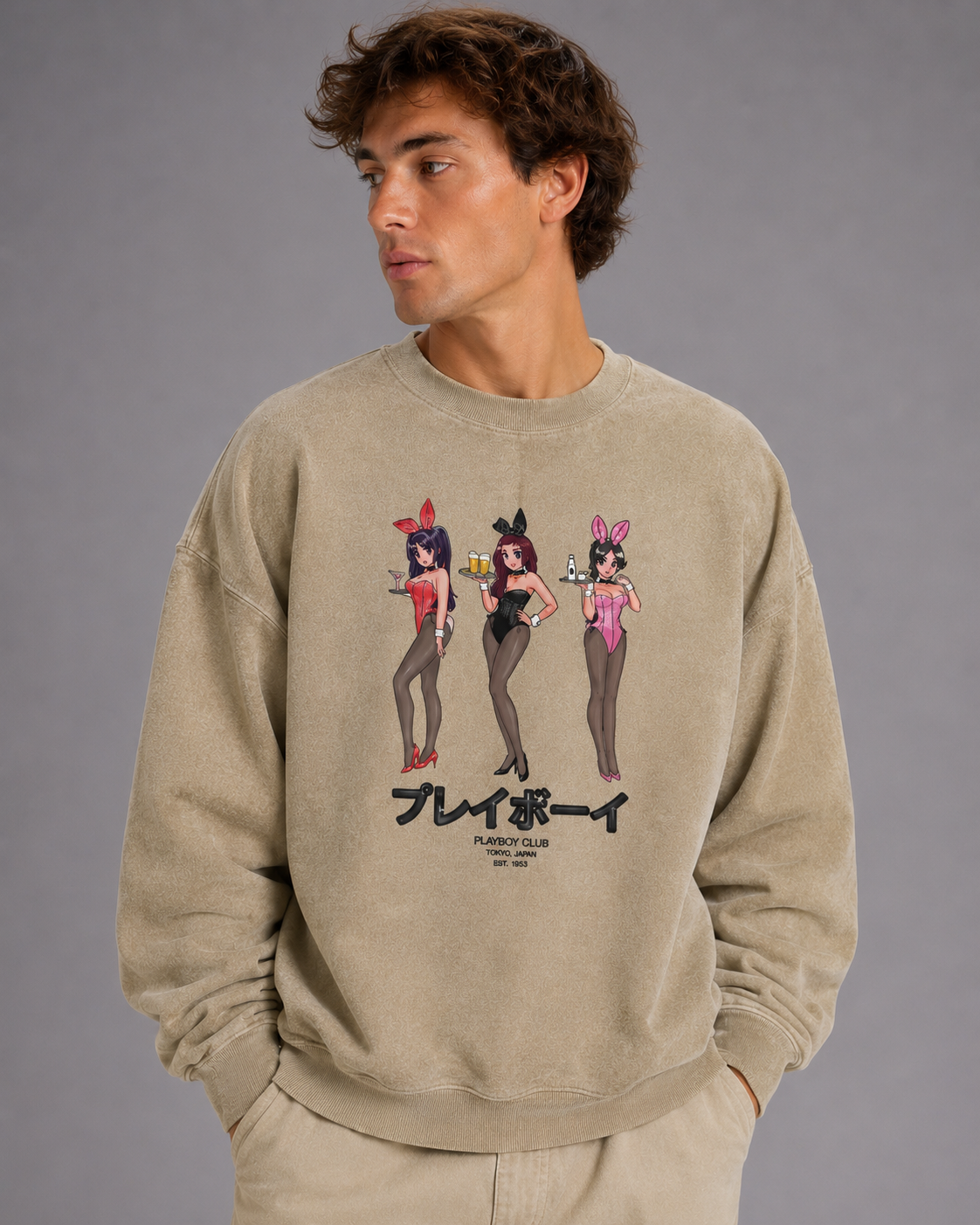 A man wearing a beige crewneck sweatshirt with a graphic print of three anime-style bunny girls and the text 'PLAYBOY' on the front, posed against a solid gray studio background.