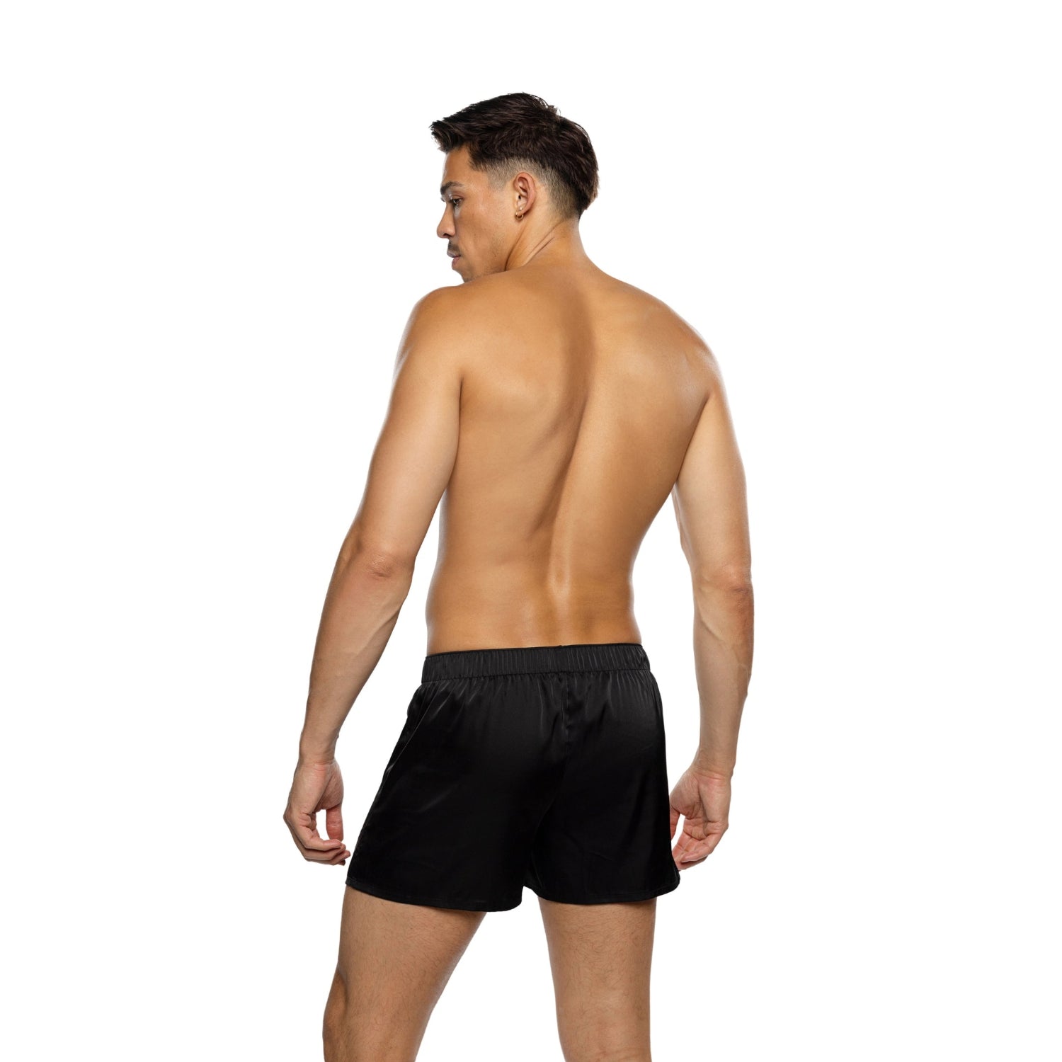 Shirtless man modeling black satin boxer shorts on white background
