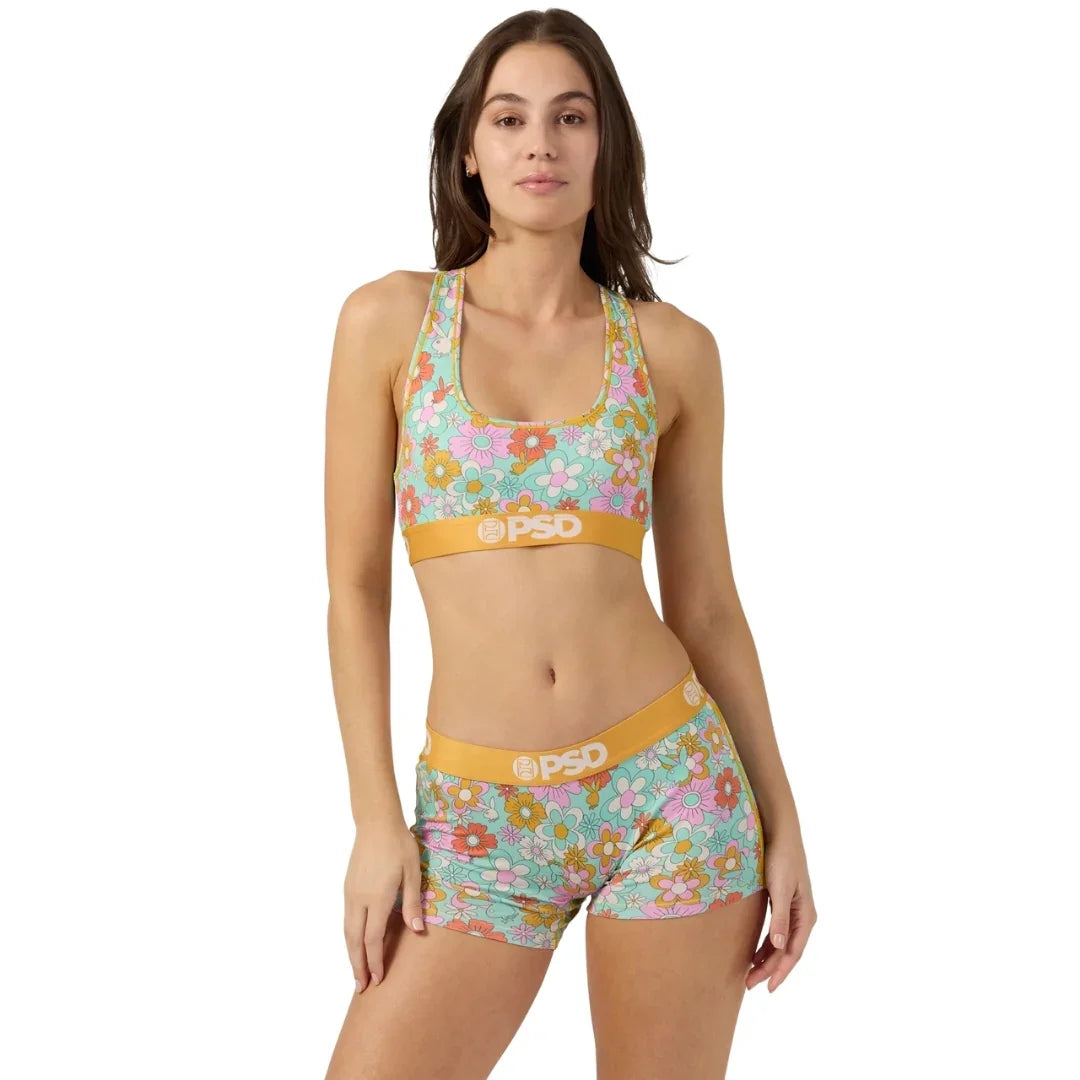 Woman wearing floral print sports bra and shorts set with yellow waistband, standing against white background
