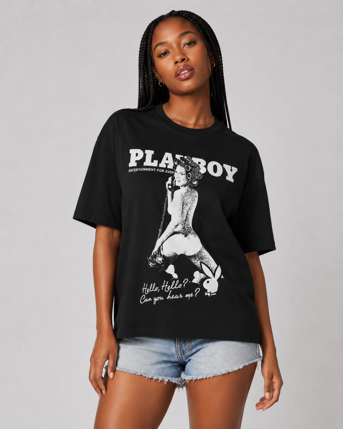 A woman modeling a black Playboy graphic t-shirt with a white print of the iconic bunny and a retro-style figure, paired with denim shorts against a neutral gray background. #Women