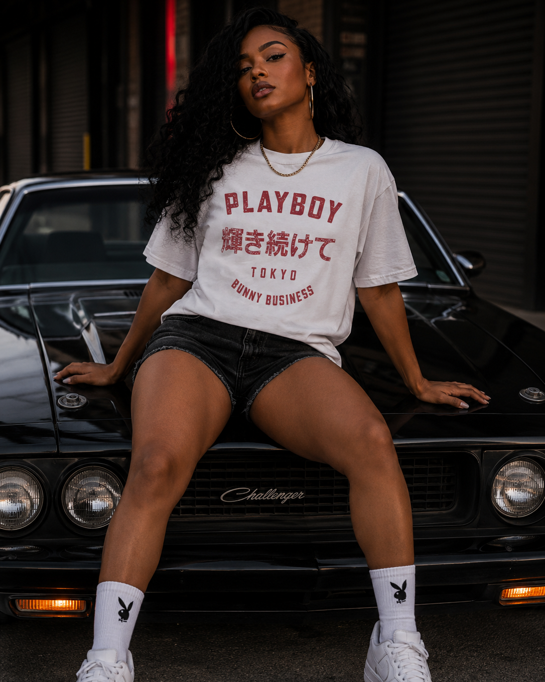 A woman sits on the hood of a black car wearing a white Playboy Tokyo t-shirt with red text, paired with white sneakers, in an urban setting. #Streetwearwomen
