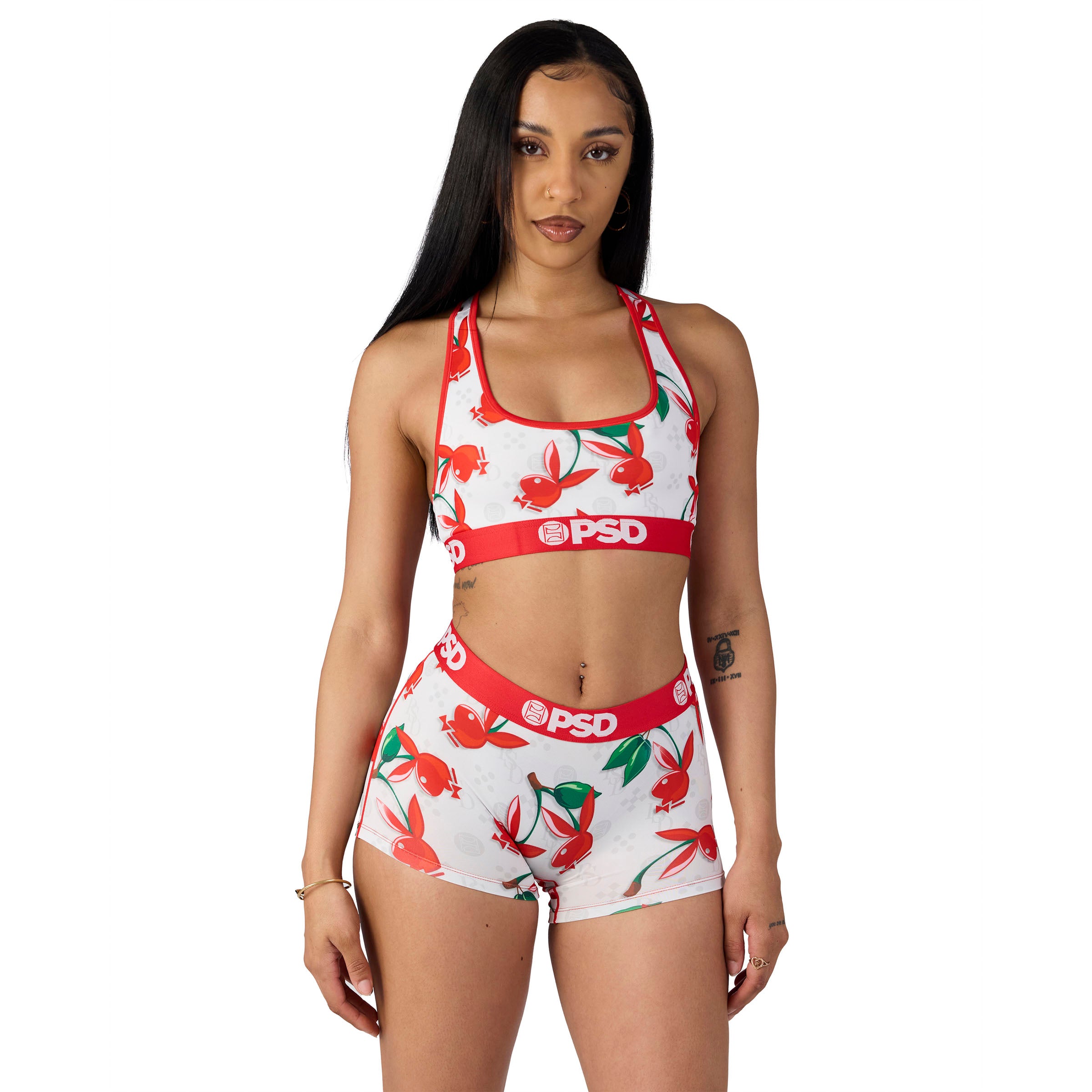 Woman modeling Playboy x PSD sports bra and shorts with red floral print on white background