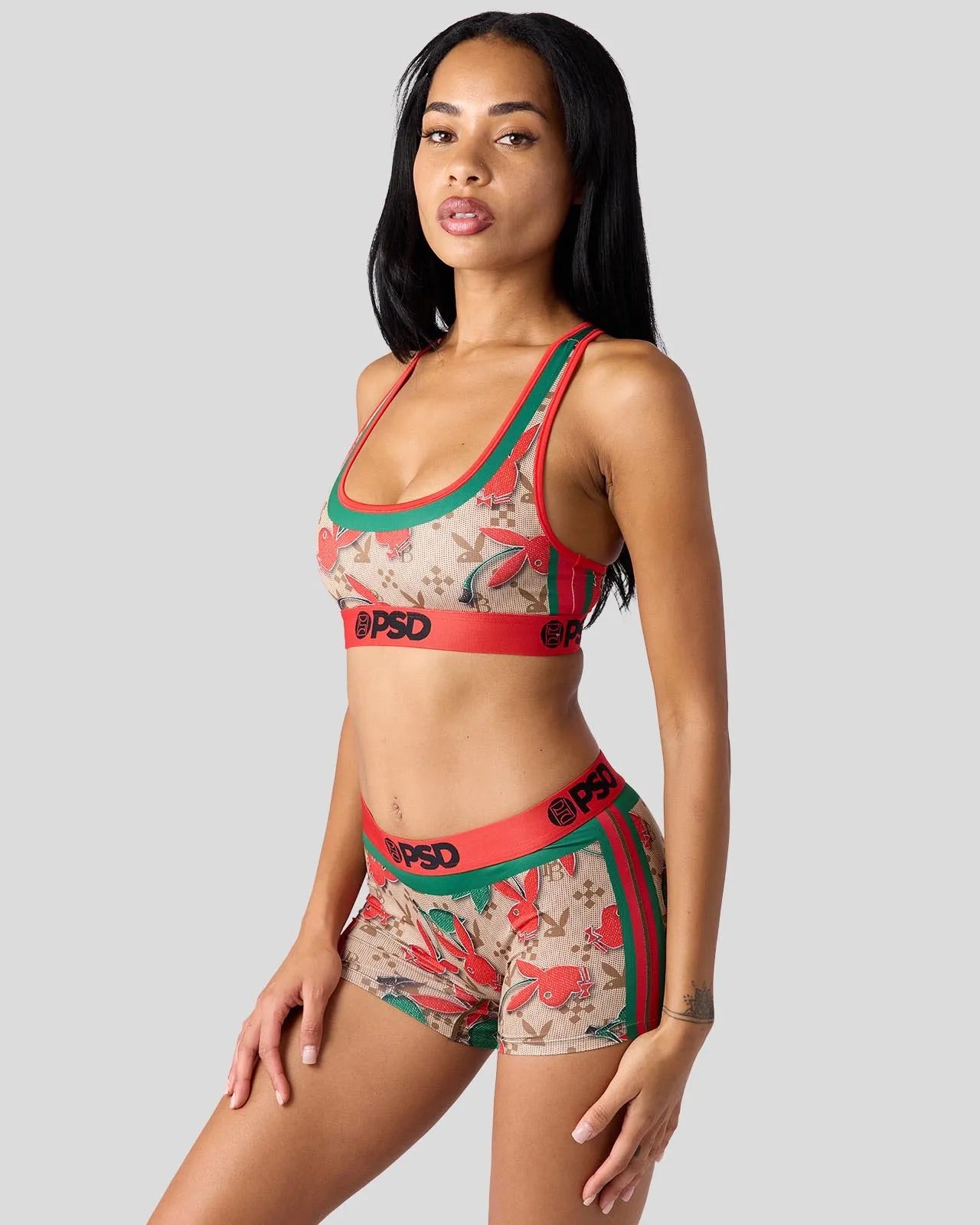 A woman modeling a matching two-piece activewear set featuring a beige and red tropical floral print with green trim and red waistbands printed with 'PSD'.