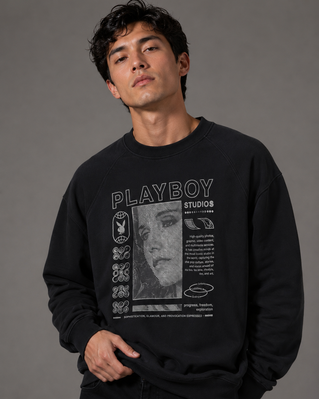A man wearing a black crewneck sweatshirt with a large white and gray Playboy Studios graphic print on the front, posed against a solid gray studio background.