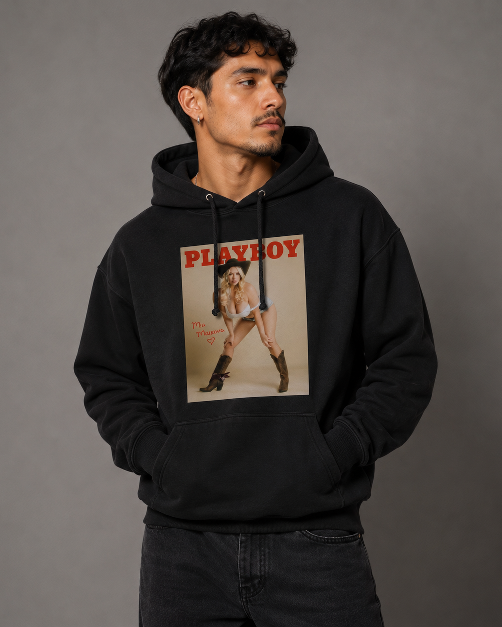 A man wearing a black pullover hoodie with a vintage-style Playboy magazine cover graphic on the front, posed against a solid gray studio background.