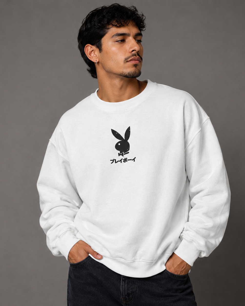 A man wearing a white crewneck sweatshirt with a black Playboy bunny logo and Japanese text on the chest, paired with dark jeans, set against a solid gray studio background.