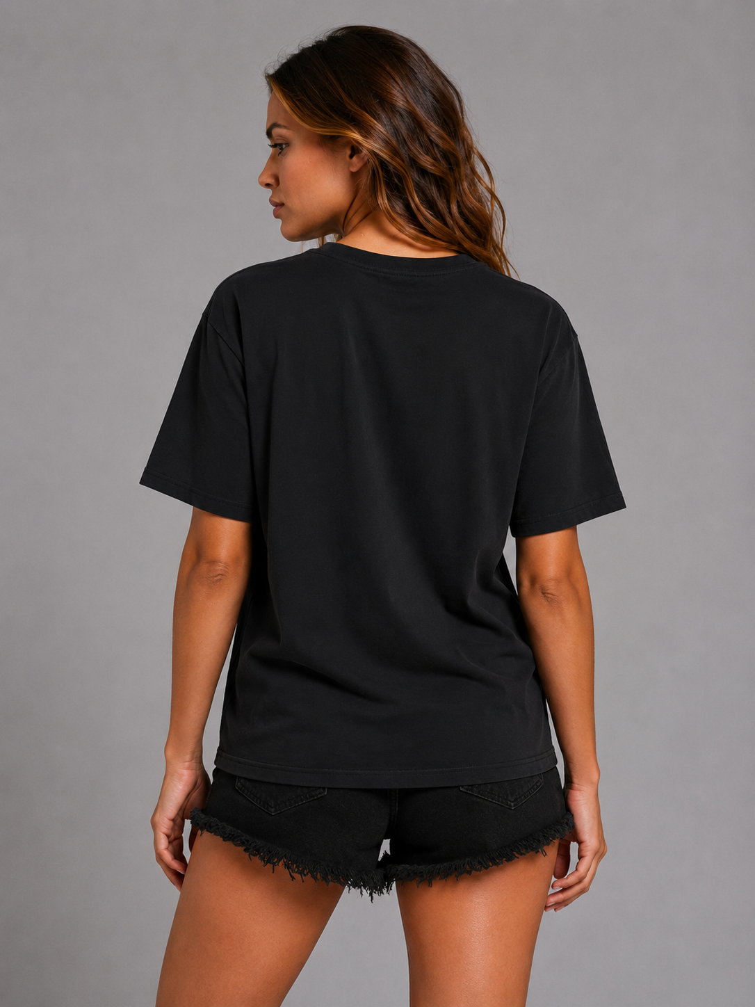 A woman shown from the back wearing a black short-sleeve t-shirt and black frayed denim shorts against a solid gray studio background.