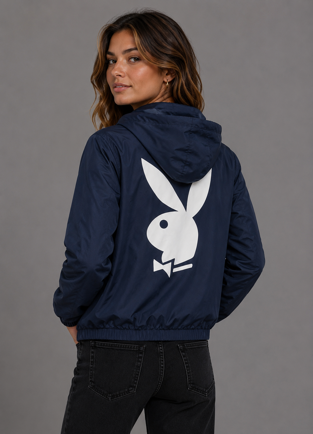 A woman wearing a navy blue hooded jacket with a large white Playboy bunny logo on the back, shown from behind against a plain gray studio background. #Women