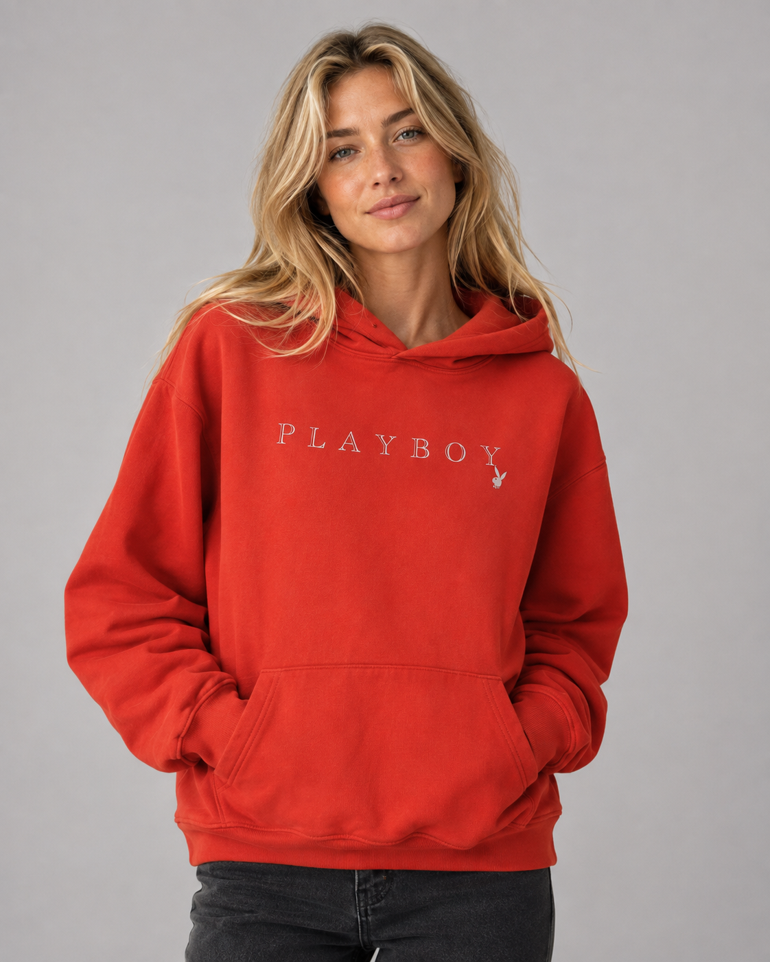 A woman wearing a bright red pullover hoodie with 'PLAYBOY' printed in white across the chest and the Playboy bunny logo on the right chest, photographed against a plain gray studio background. #Women