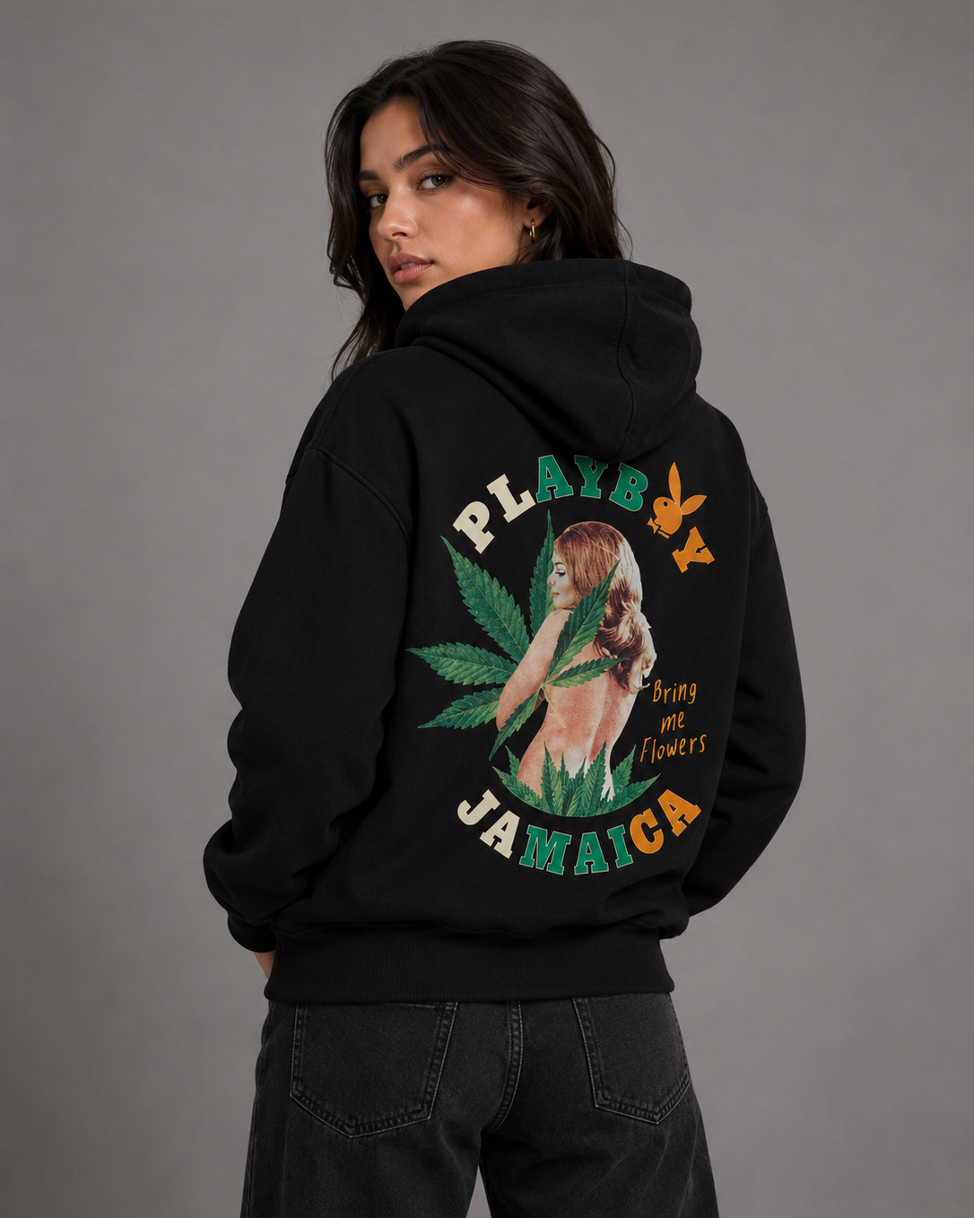 A woman wearing a black hoodie with a large back graphic featuring the text 'PLAYBOY JAMAICA', a green cannabis leaf, and a vintage-style illustrated woman, shown against a plain gray studio background. #Women