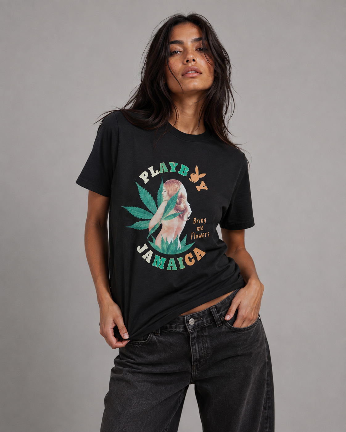 A woman modeling a black graphic t-shirt with a colorful print featuring a mermaid, a cannabis leaf, and the text 'PLAYS JAMAICA' and 'Breat or Flowers'. She is wearing dark gray jeans against a solid gray studio background. #Women