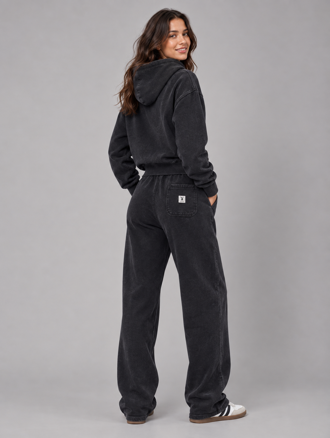A woman wearing a matching black hooded sweatshirt and wide-leg sweatpants, photographed from the back against a solid gray studio background. #Women