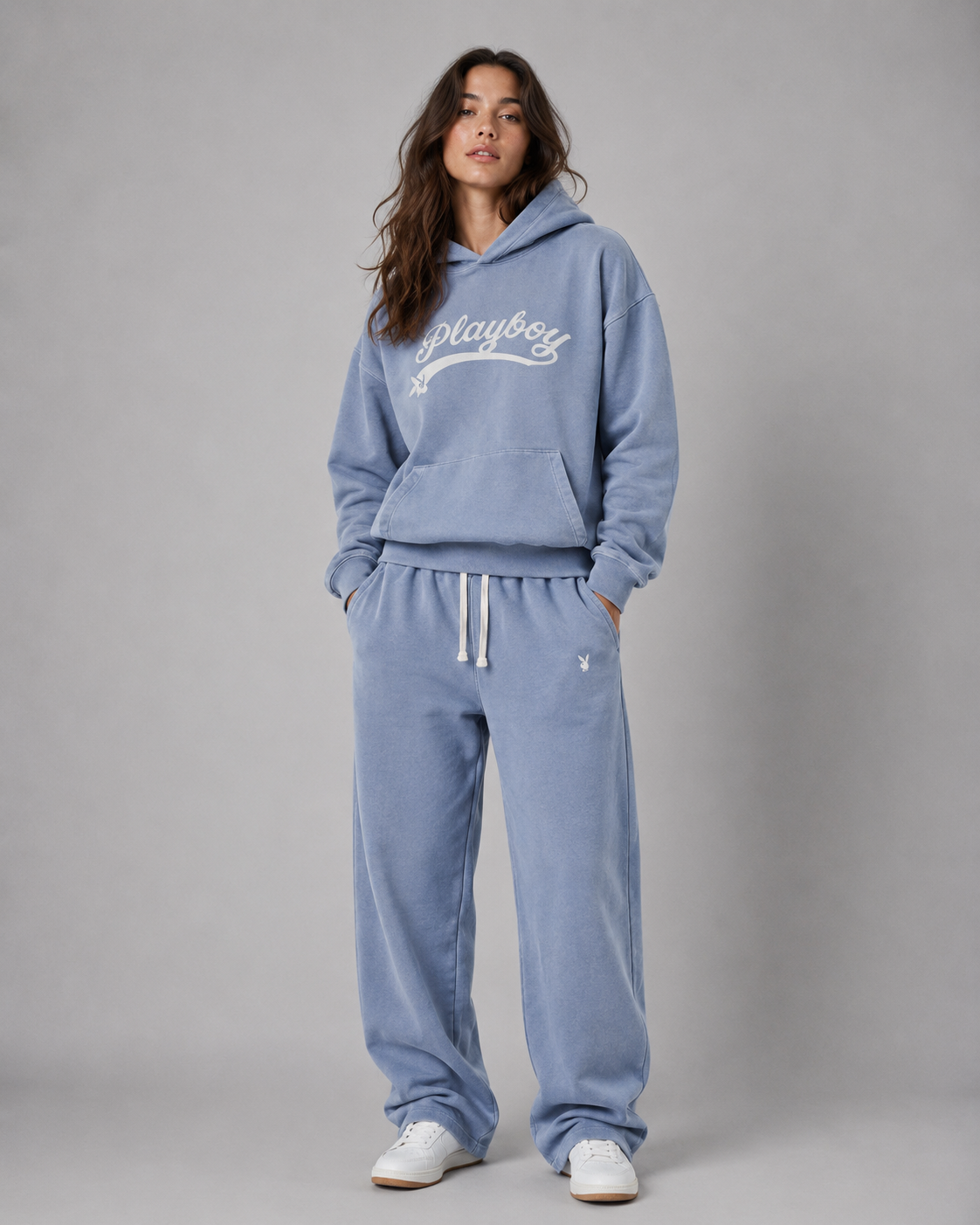 A woman modeling a light blue fleece loungewear set consisting of a hoodie with a white 'Playboy' script logo on the chest and matching sweatpants with white drawstrings, set against a plain gray studio background. #Women