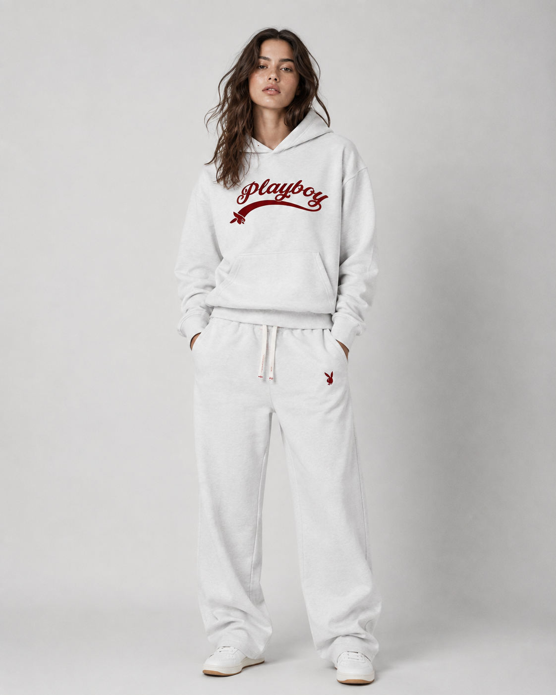 A woman modeling a white Playboy lounge set consisting of a pullover hoodie and matching sweatpants, featuring the red Playboy logo on the chest and thigh. #Women