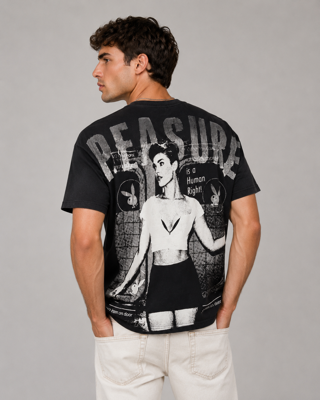 A man wearing a black graphic t-shirt with a large white and gray print on the back, featuring the word 'DEPLETE' and a stylized illustration, paired with off-white pants, photographed against a neutral gray background.