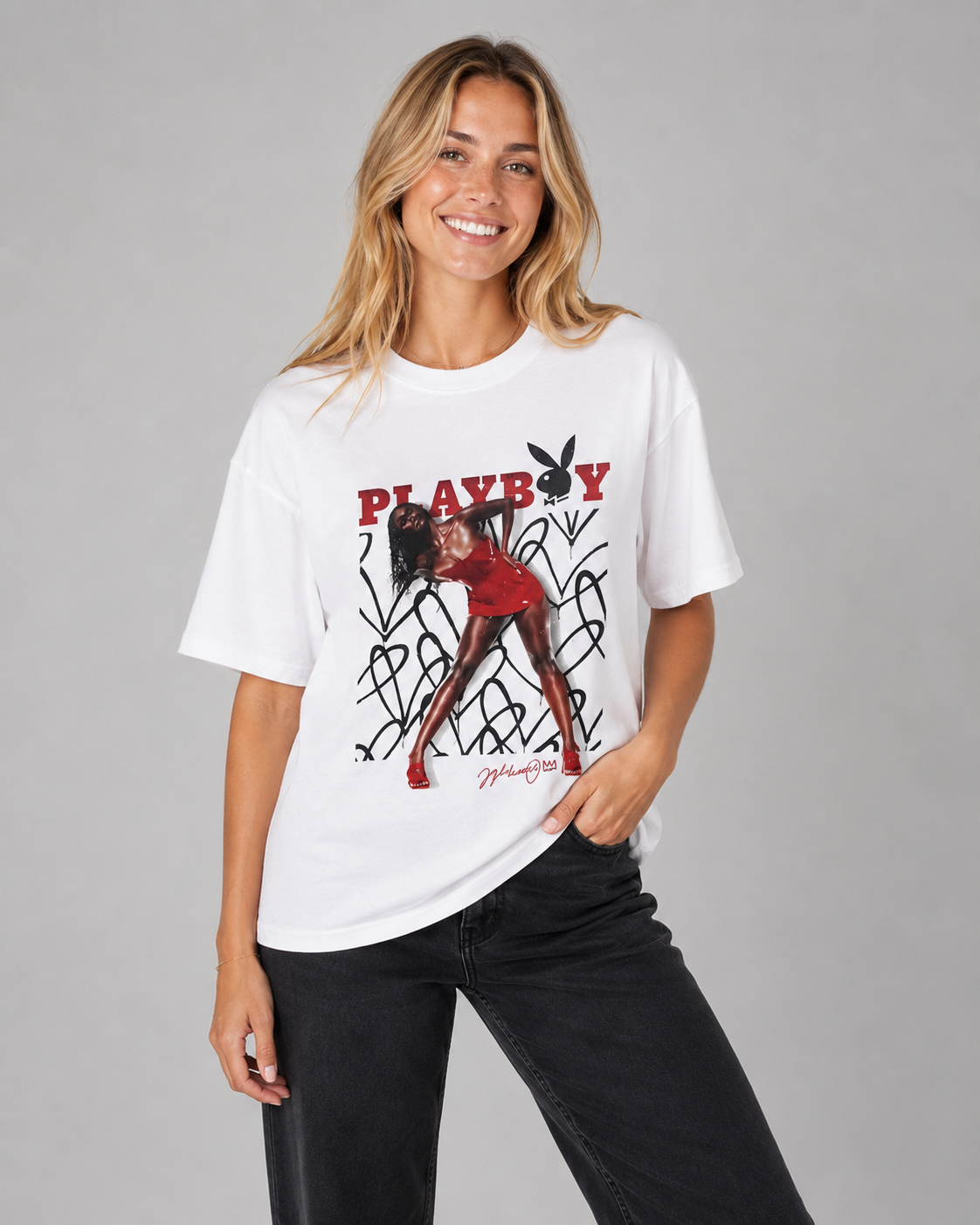 A woman modeling a white Playboy graphic t-shirt with a red and black design, paired with black jeans, against a solid gray studio background. #Women