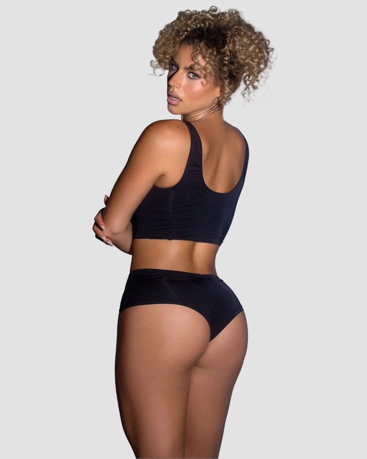 Woman wearing black 2-piece lounge set, crop tank top and boyshorts, back view.