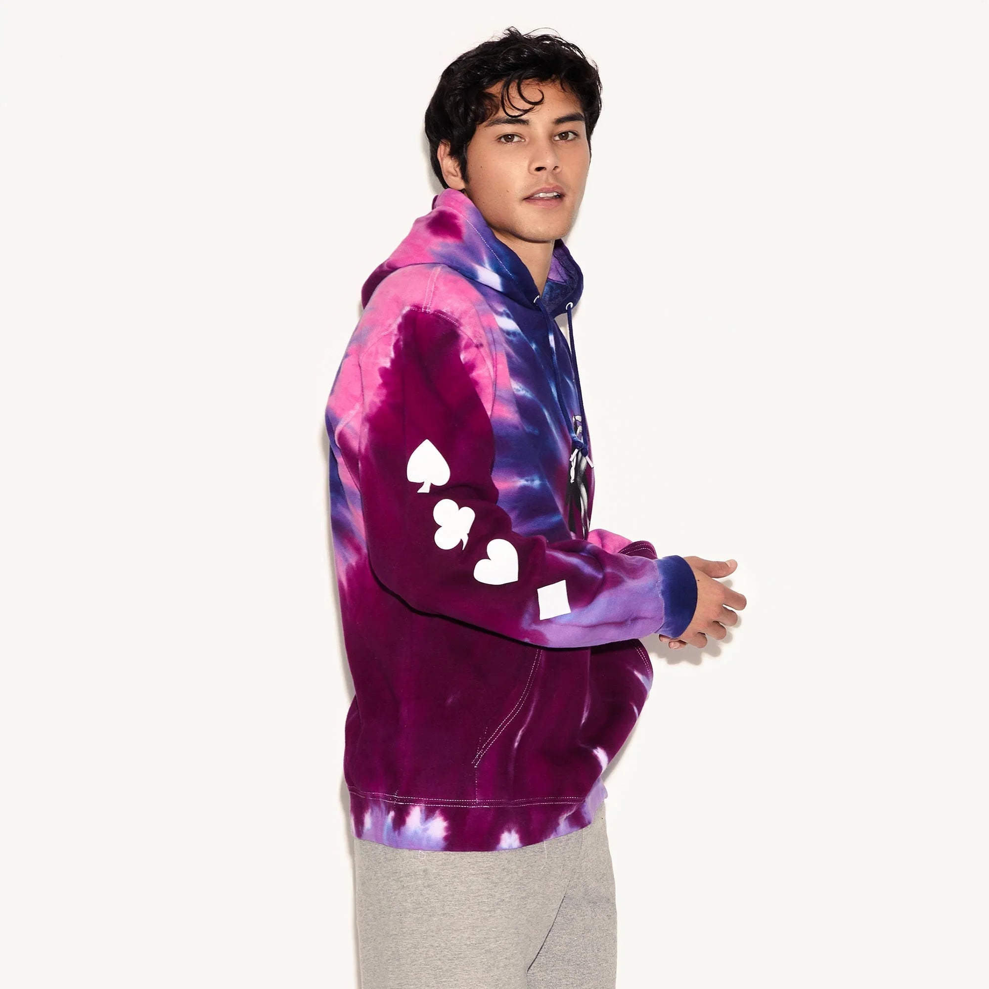 Man wearing a purple and blue tie-dye hoodie with white playing card suit symbols on the sleeve