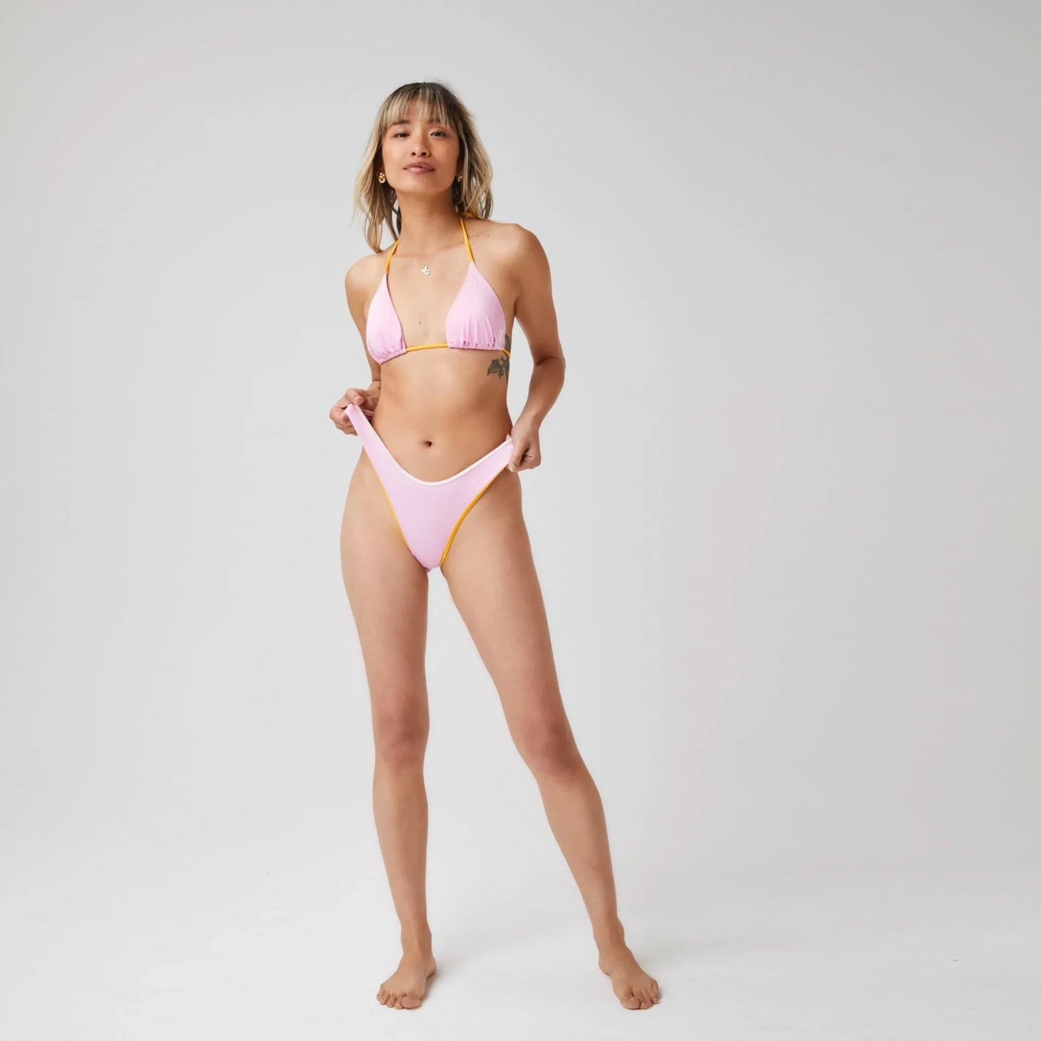 Woman wearing light pink adjustable triangle bikini top and matching high-leg bottoms in studio