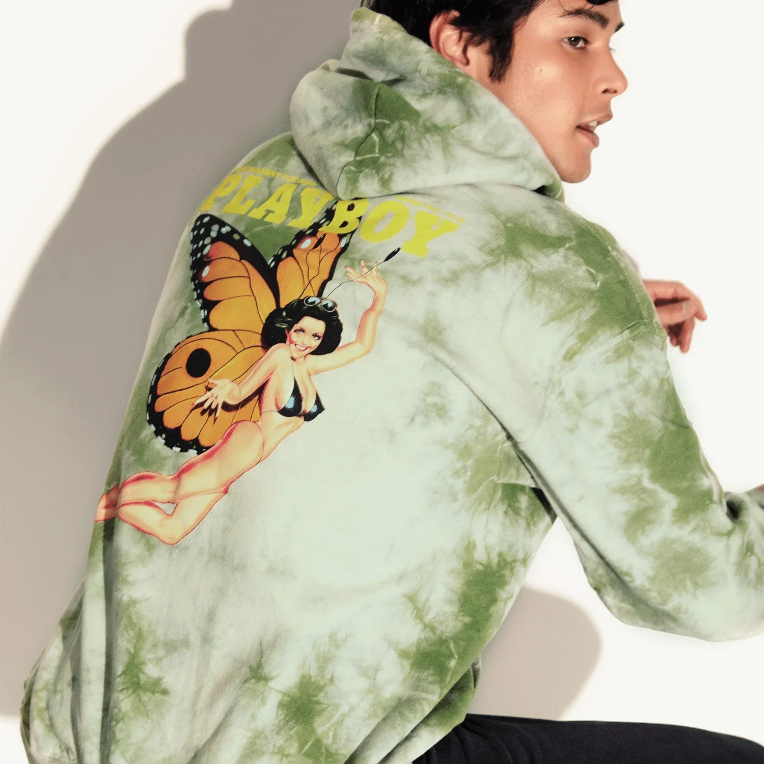 Man wearing green tie-dye hoodie with vintage butterfly bikini graphic and bold yellow text on back