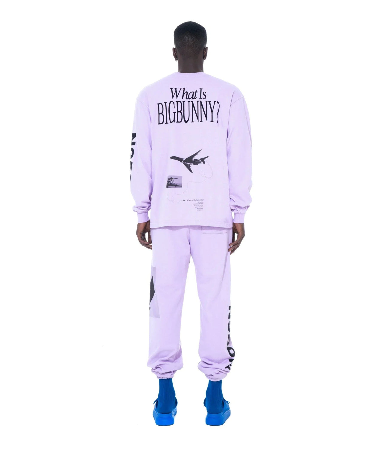 Man wearing lavender long sleeve shirt and sweatpants with airplane and text graphic on back