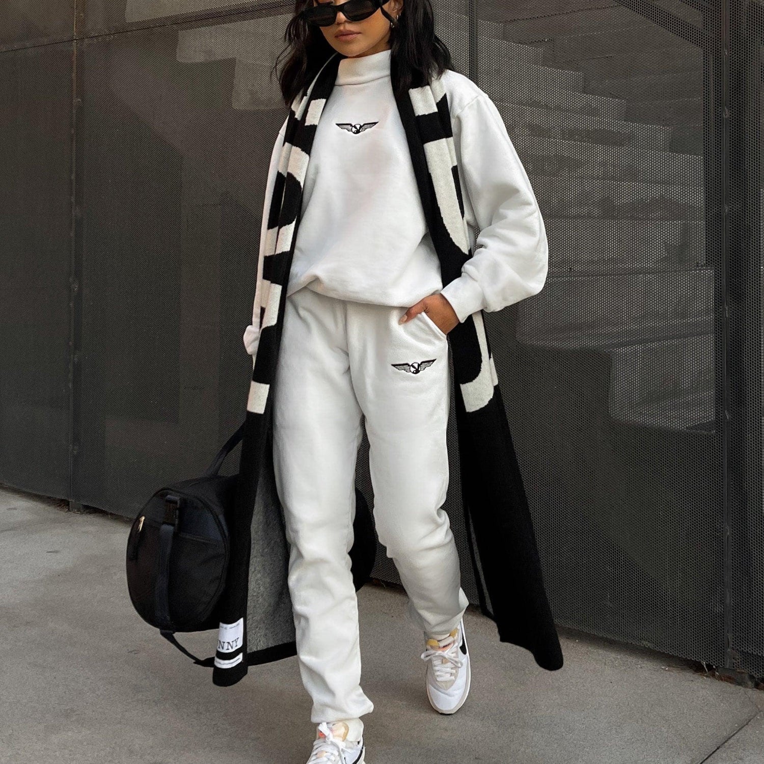 Woman in white aviation wings sweatpants, matching sweatshirt, black and white scarf, casual street style
