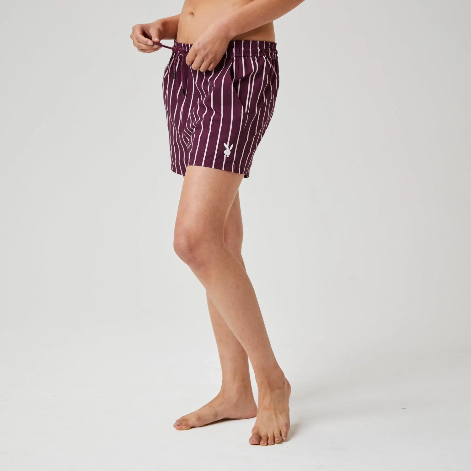 Person wearing maroon pinstripe board shorts with white logo on left leg, plain background