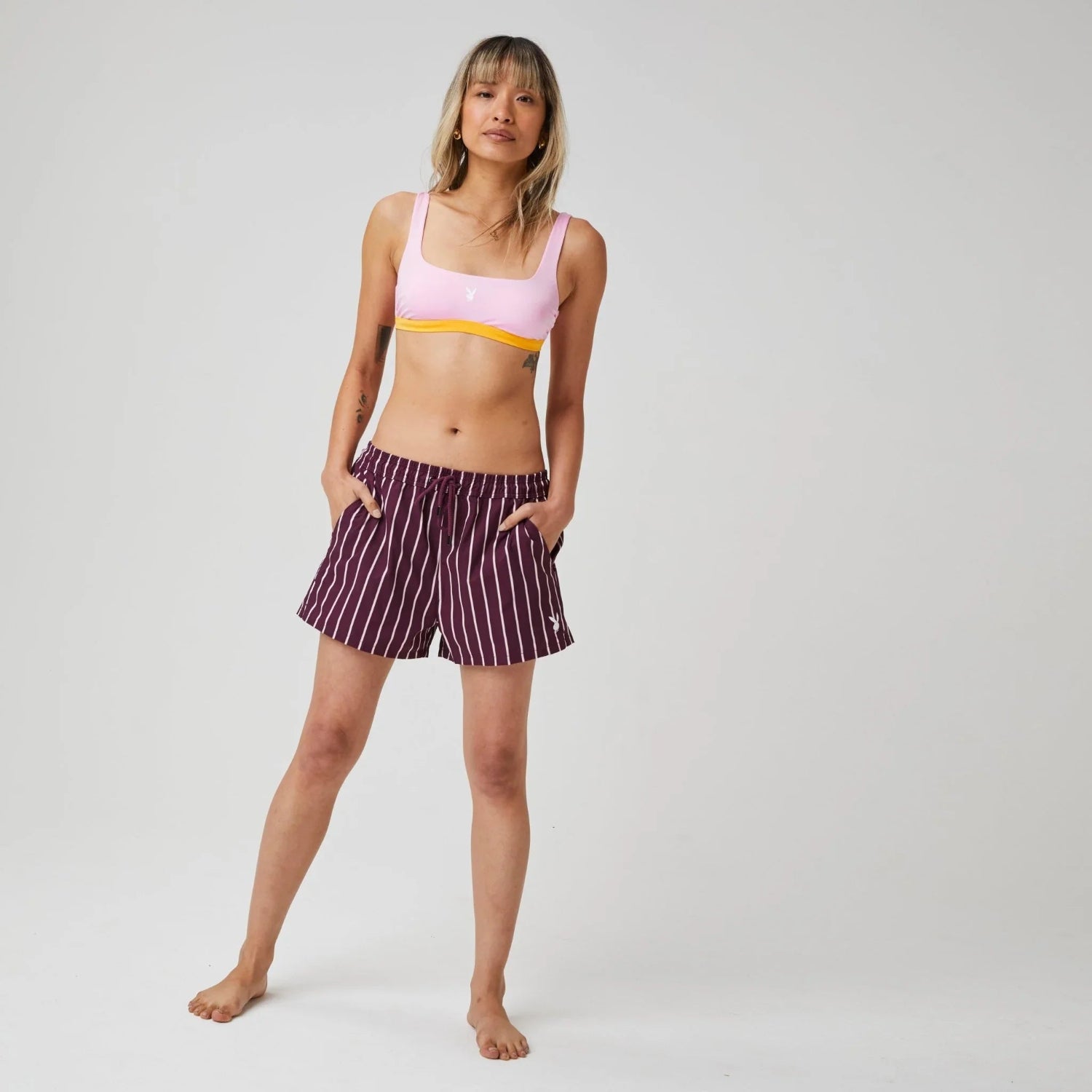 Woman modeling pink bikini top and maroon striped board shorts with drawstring waist