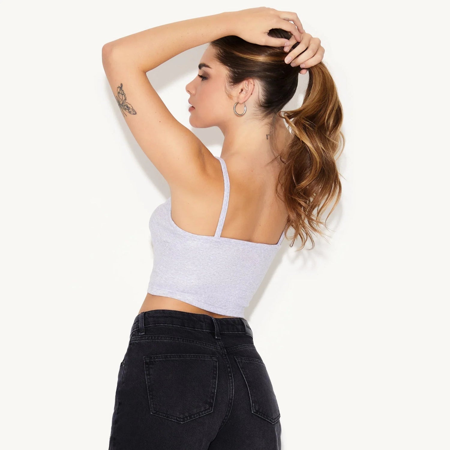 Woman wearing light grey cami crop top and black high-waisted jeans, pose from back