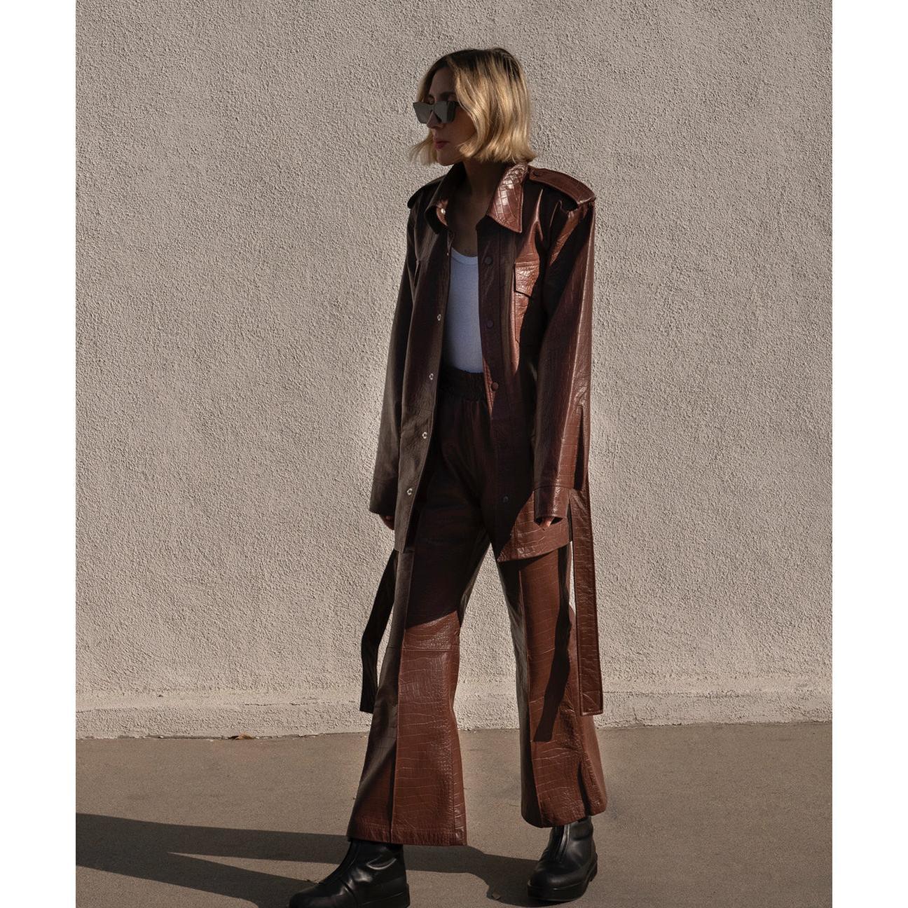 Woman wearing brown crocodile leather flare pants and matching jacket, white top, black boots