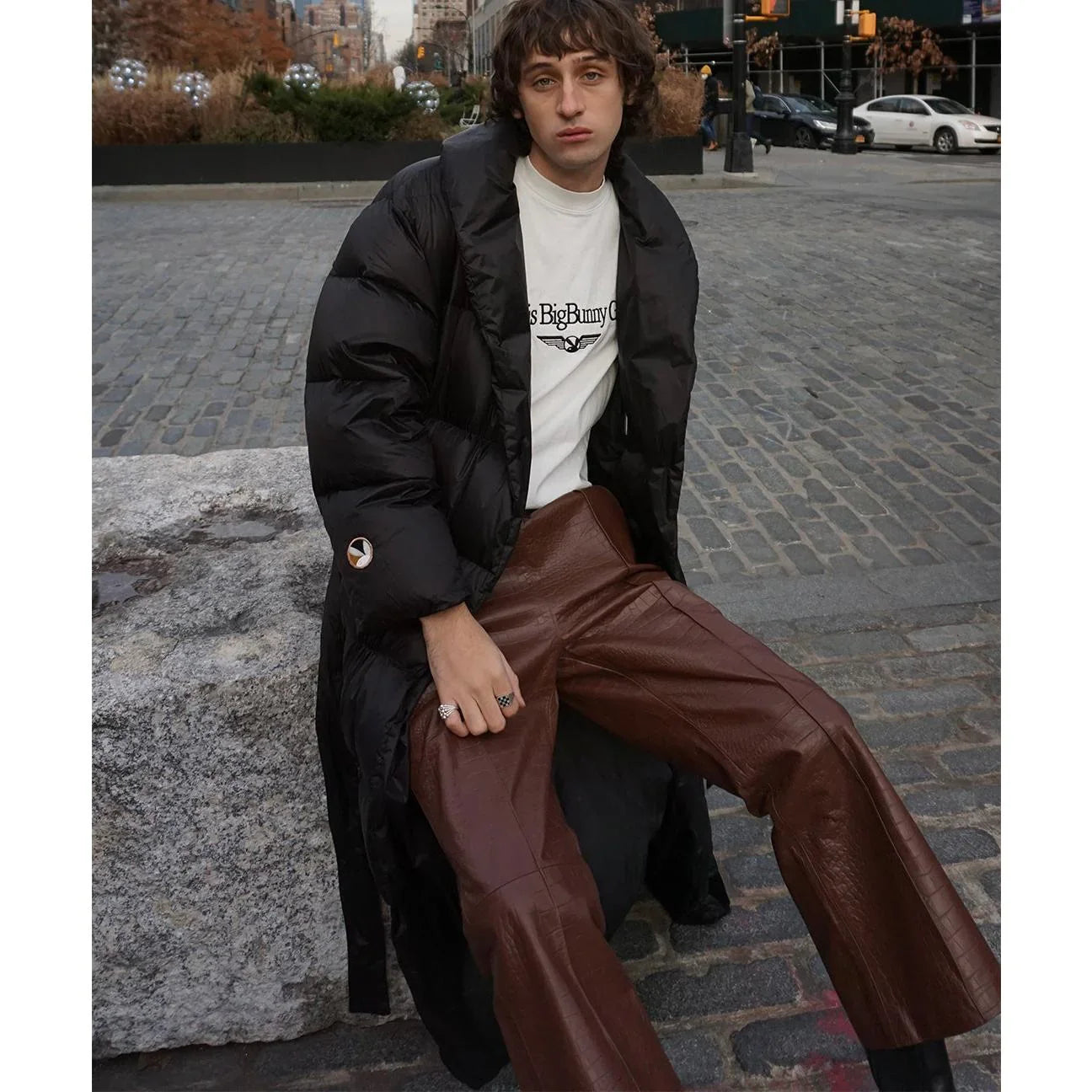 Person wearing crocodile-embossed brown leather flare pants, puffer coat, and graphic tee on city street