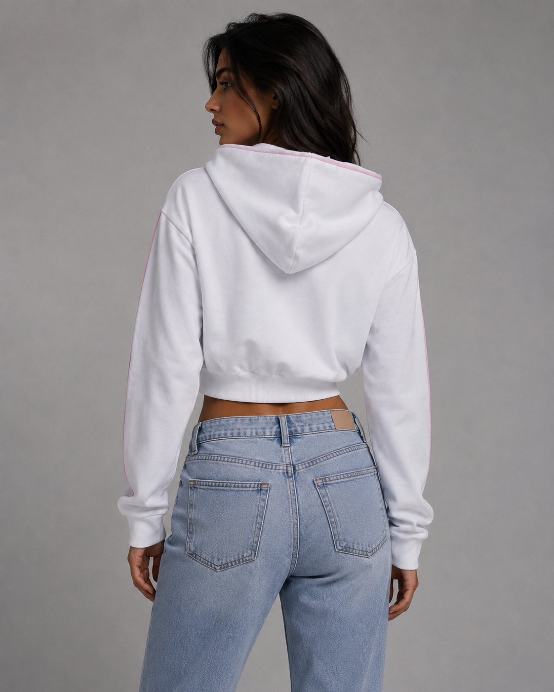 A woman shown from the back wearing a white cropped hoodie with a light pink inner hood lining and light-wash blue jeans, against a plain gray studio background. #Women