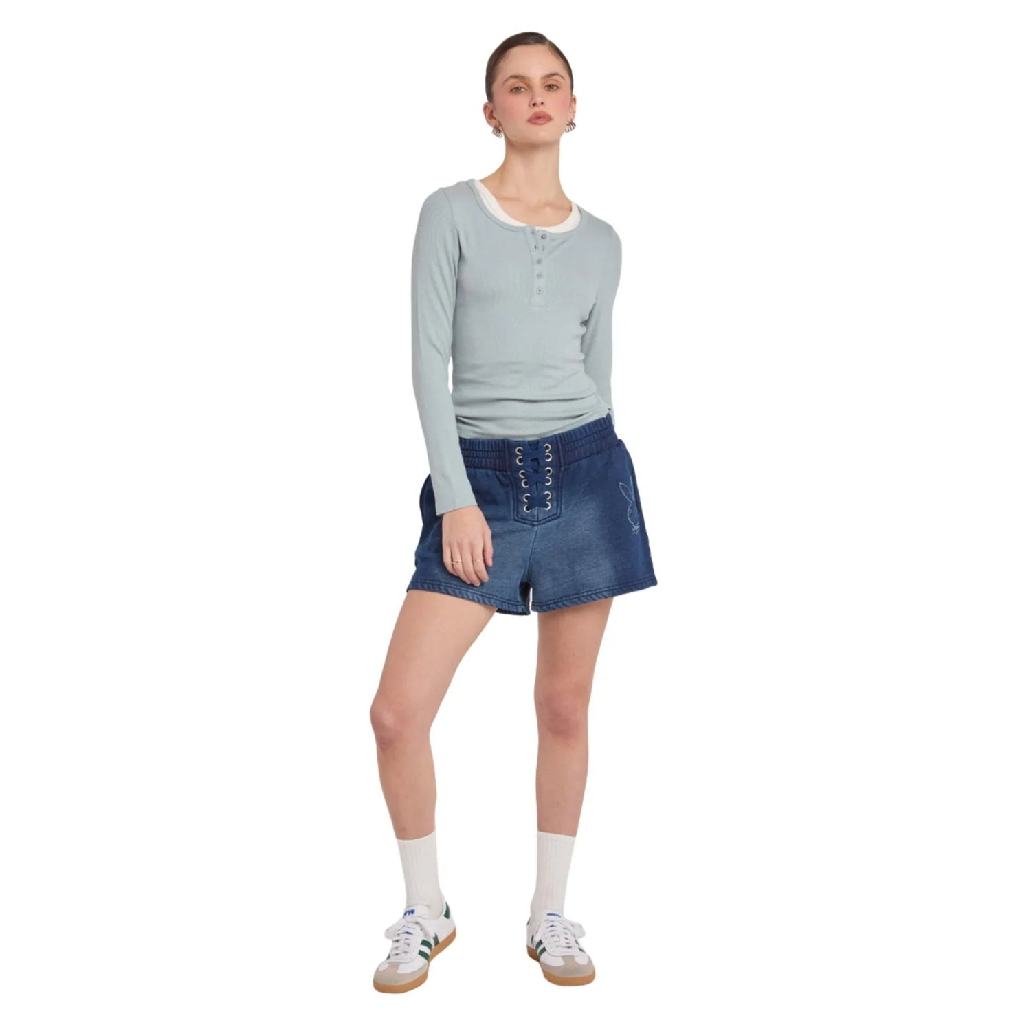 Woman wearing blue lace-up denim shorts, light long sleeve top, and white sneakers