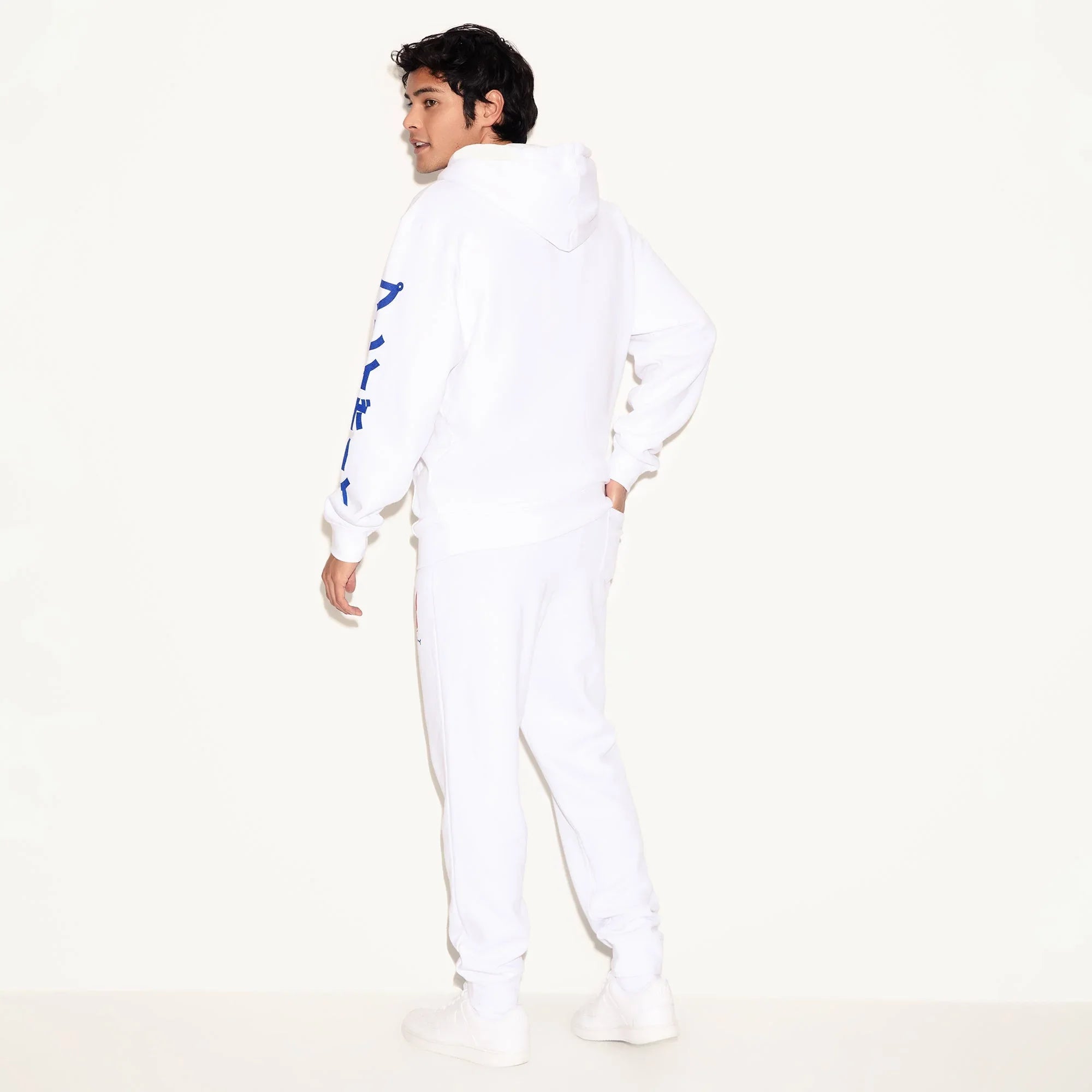 Man wearing white hoodie with blue Japanese text on sleeve, matching white joggers, white shoes