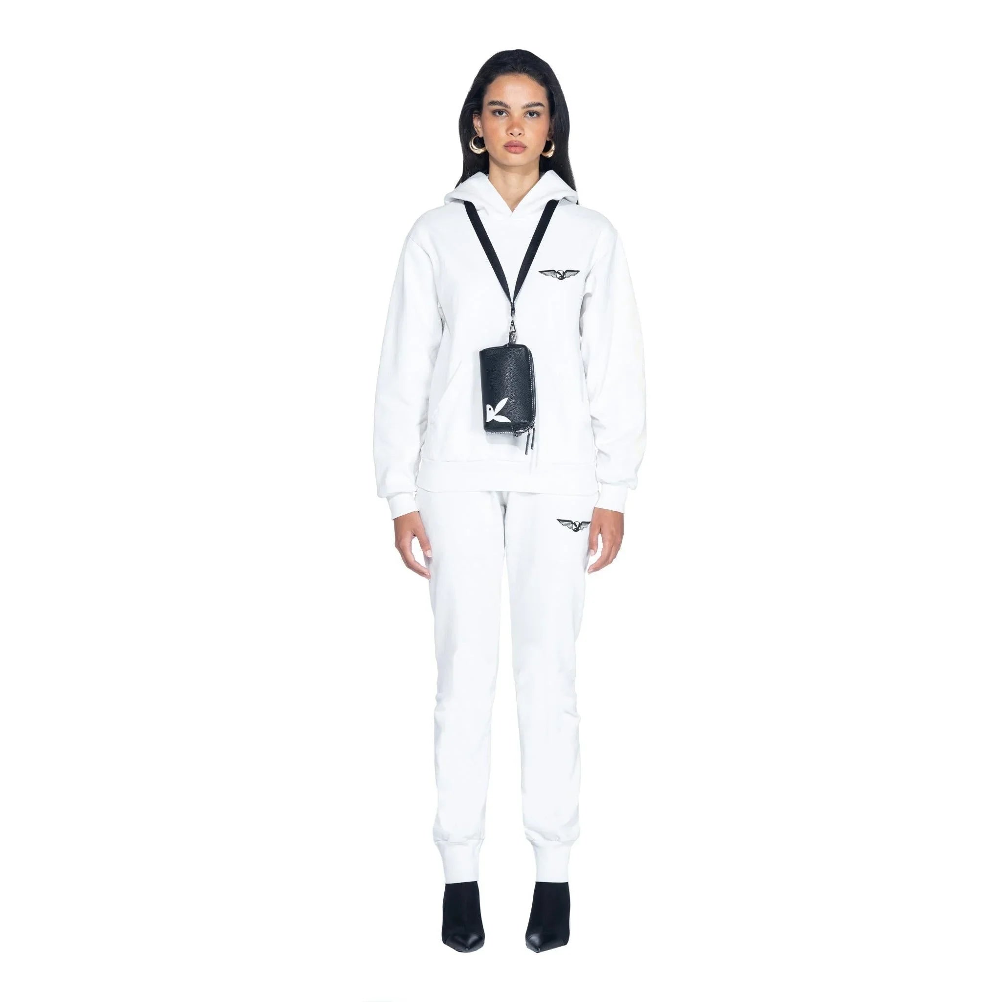 Woman in white tracksuit with black leather pouch crossbody bag featuring graphic logo.