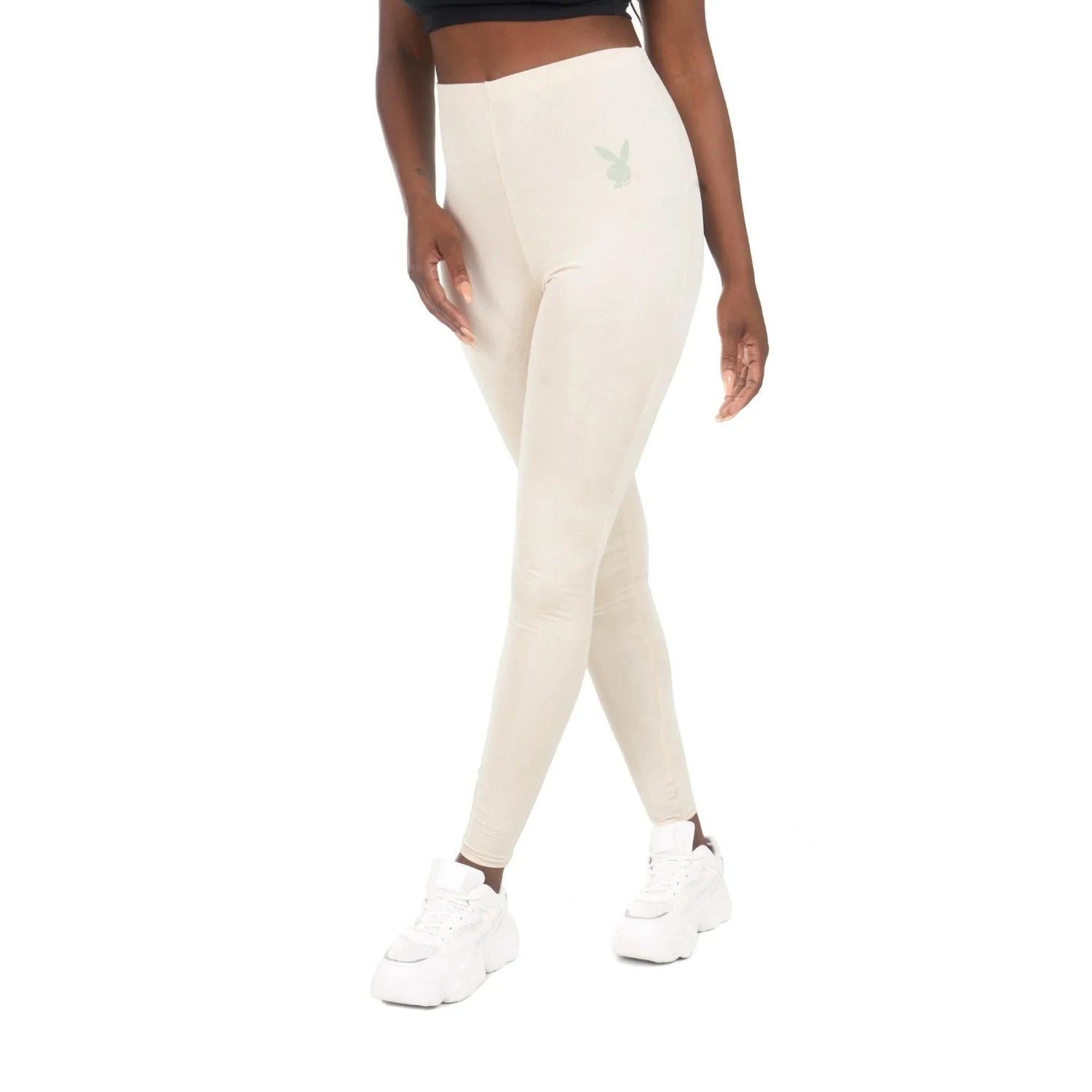 Woman wearing high-waisted beige leggings with bunny logo, white sneakers, white background