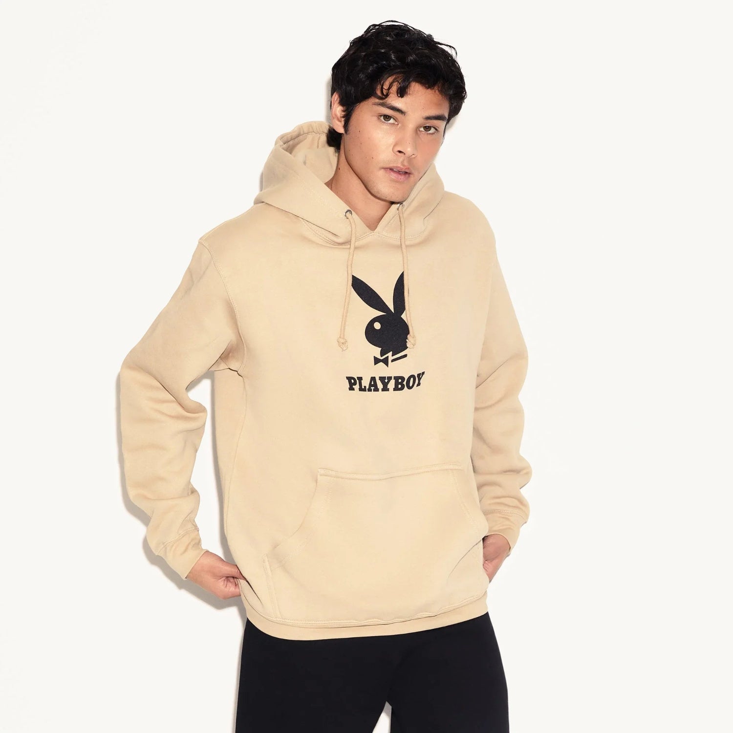 Man wearing beige hoodie with black Playboy bunny logo and front pocket