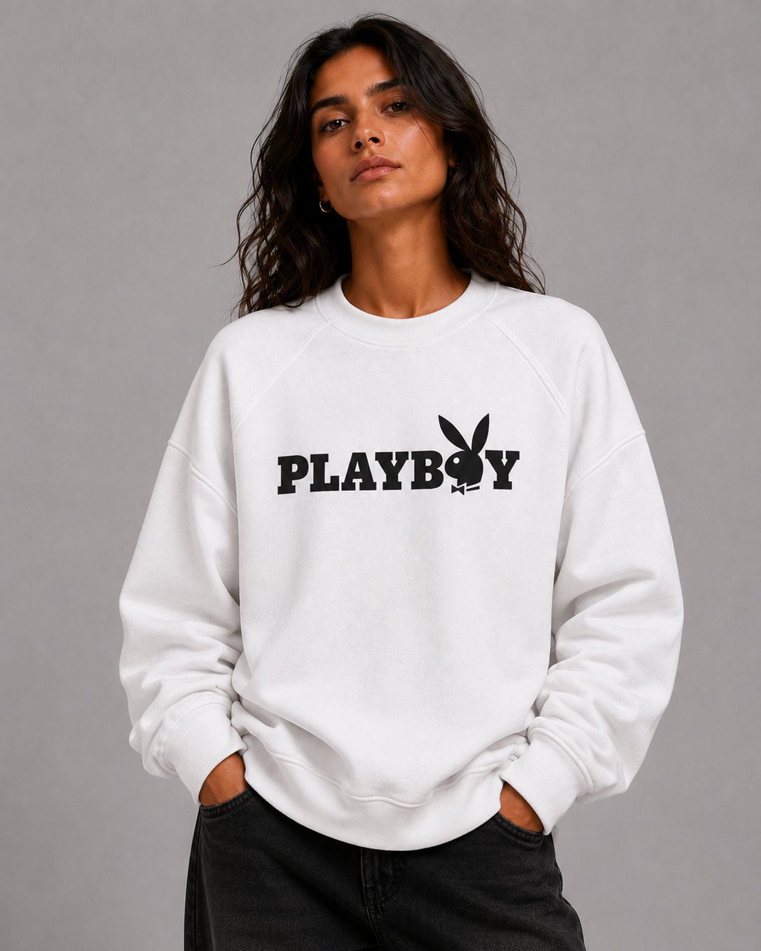 A woman wearing a white crewneck sweatshirt with a black PLAYBOY logo and bunny graphic on the chest, paired with black jeans, against a solid gray studio background. #women