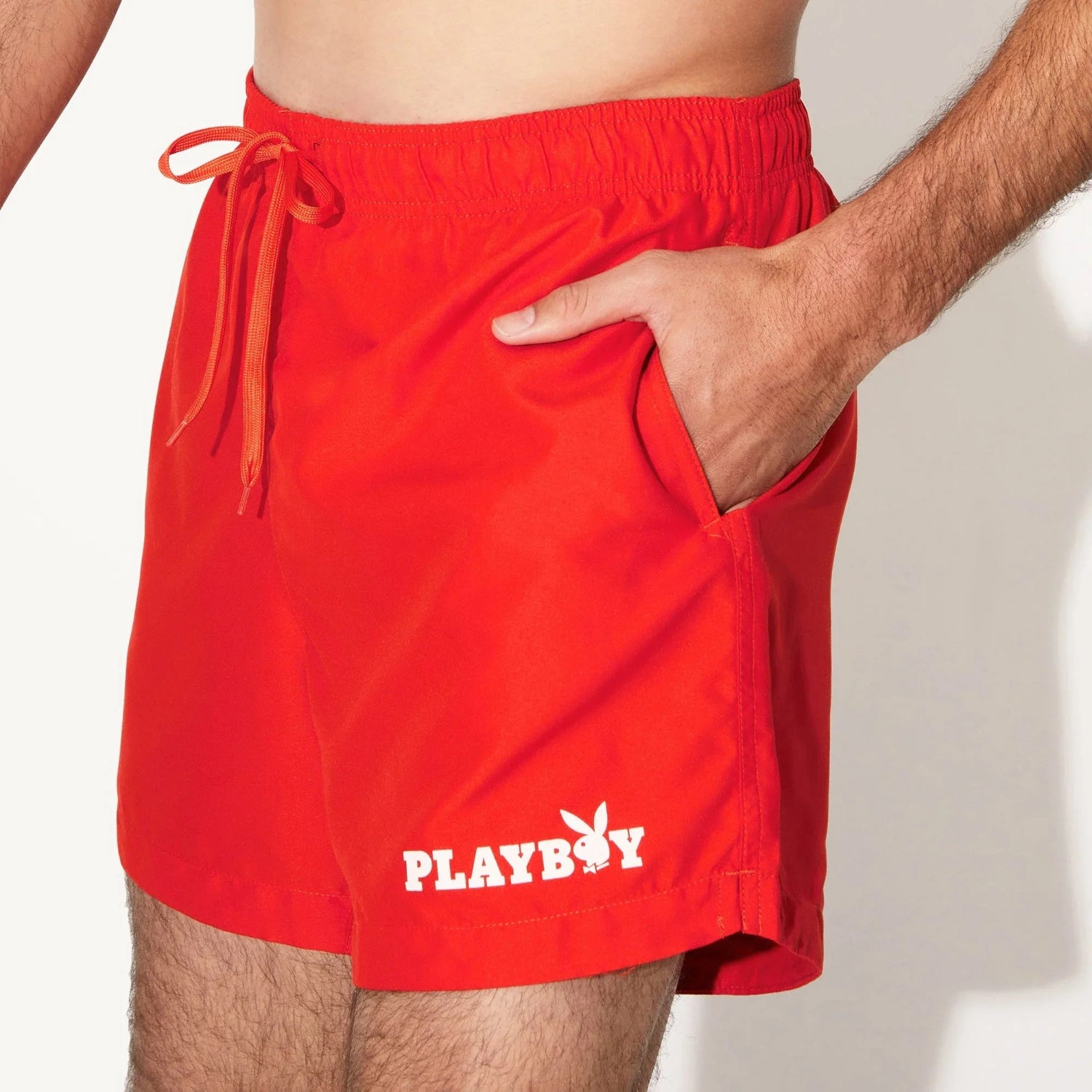Men's red swim trunks with elastic waistband, drawstring, side pocket, and bold white logo print