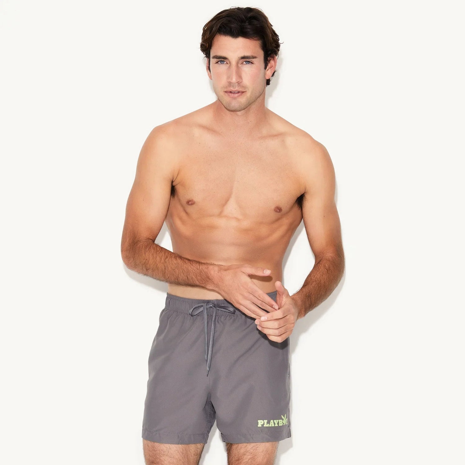 Man modeling gray men's swim trunks with drawstring and small yellow graphic on left leg