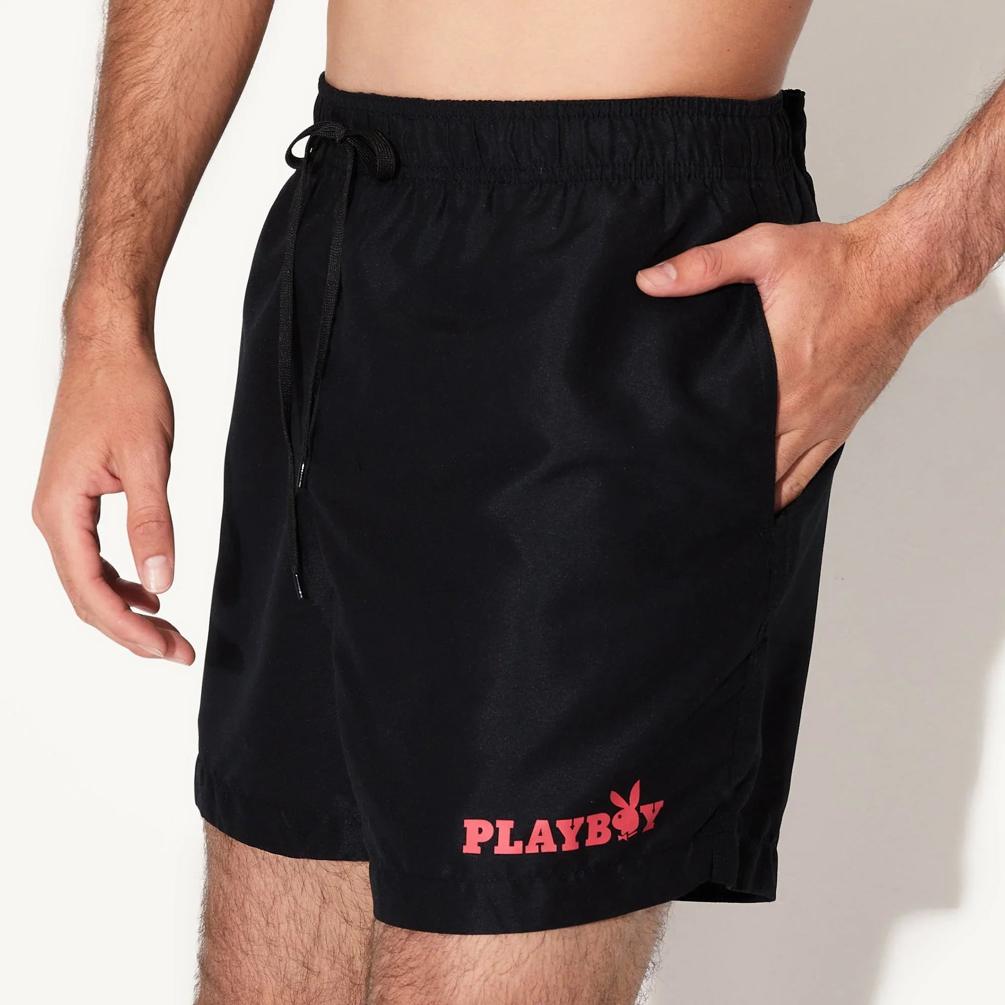 Man wearing black swim trunks with red Playboy logo and drawstring waistband