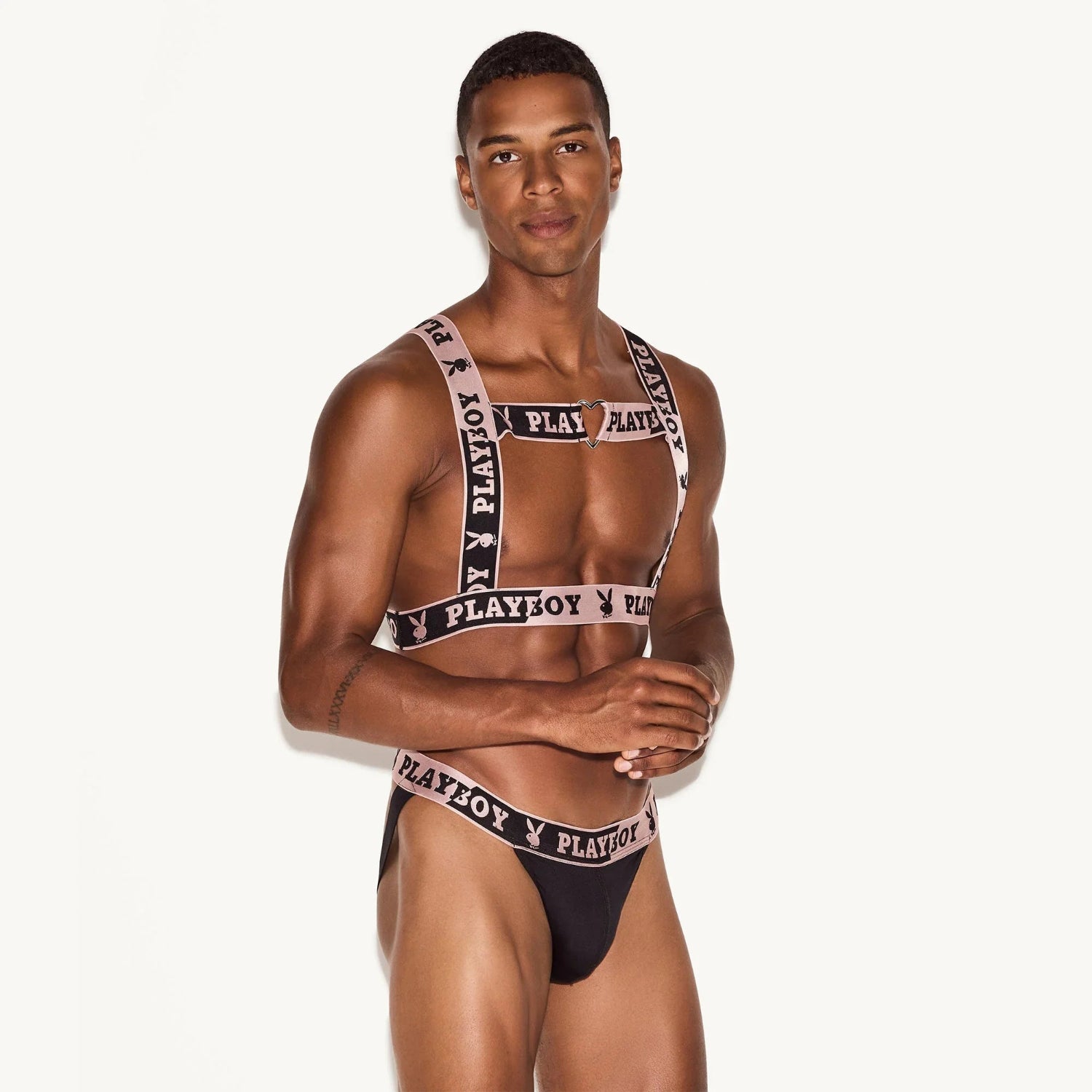 Male model in black harness and briefs set with heart detail and pink Playboy logo trim