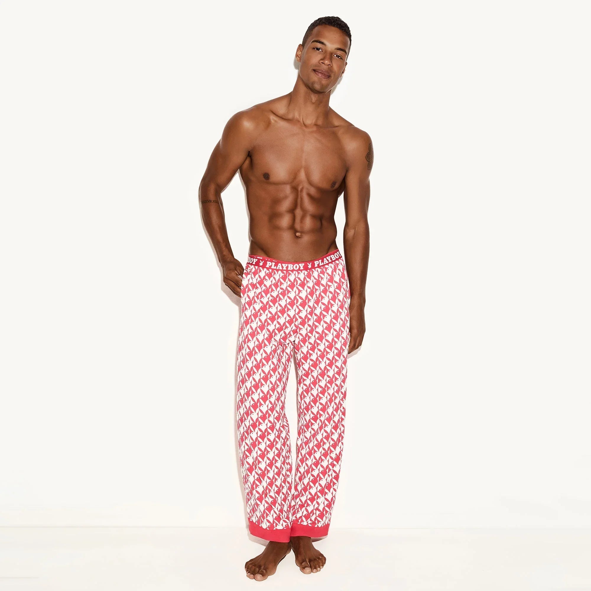 Man wearing red and white bunny print men's pajama pants with logo waistband, standing barefoot.