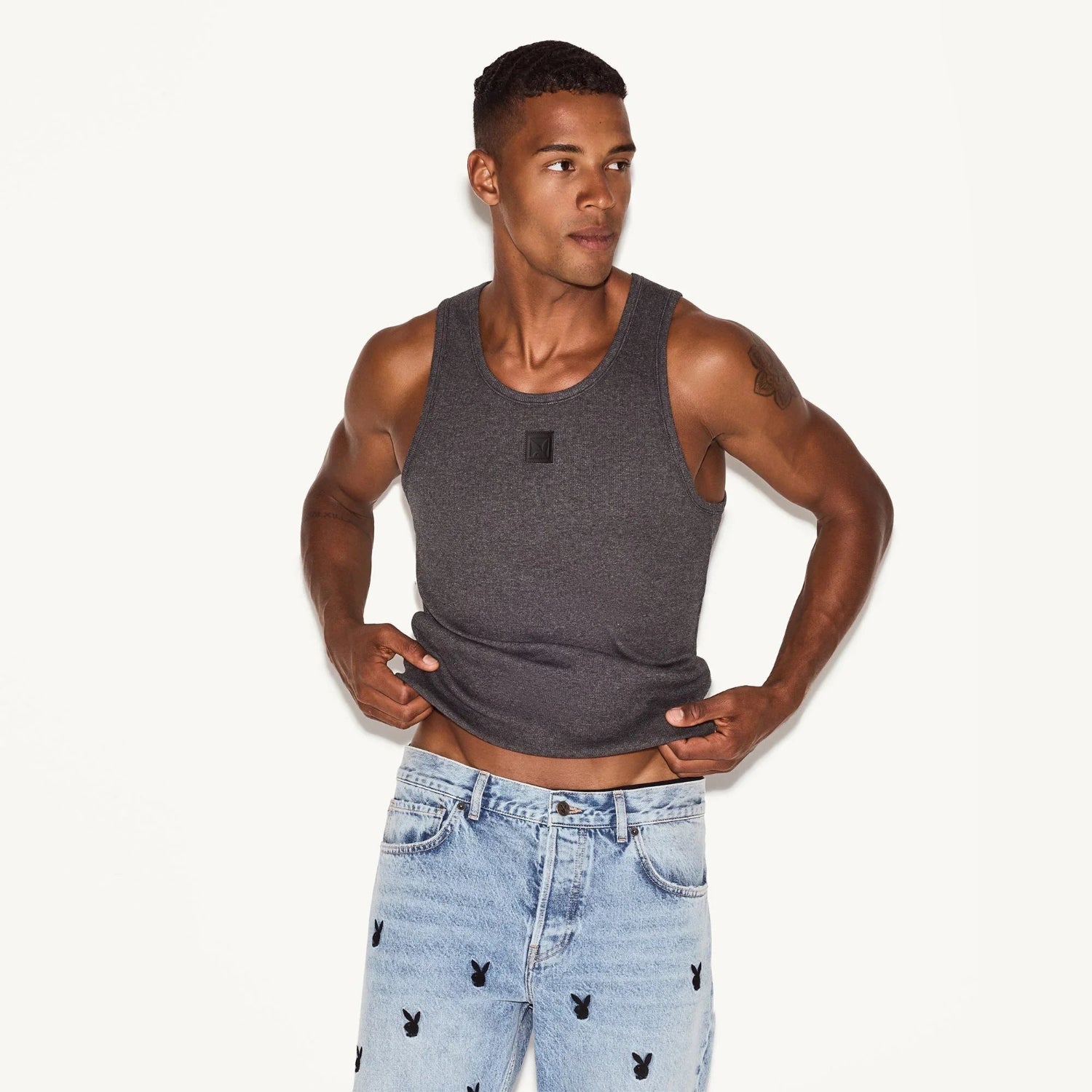 Male model wearing a charcoal rib tank top and light wash jeans with bunny logos.