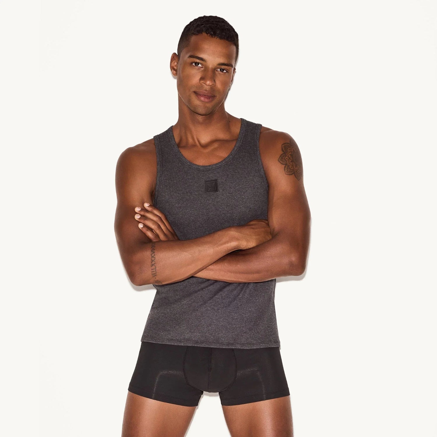 Man modeling dark gray ribbed tank top and black boxer briefs against white background