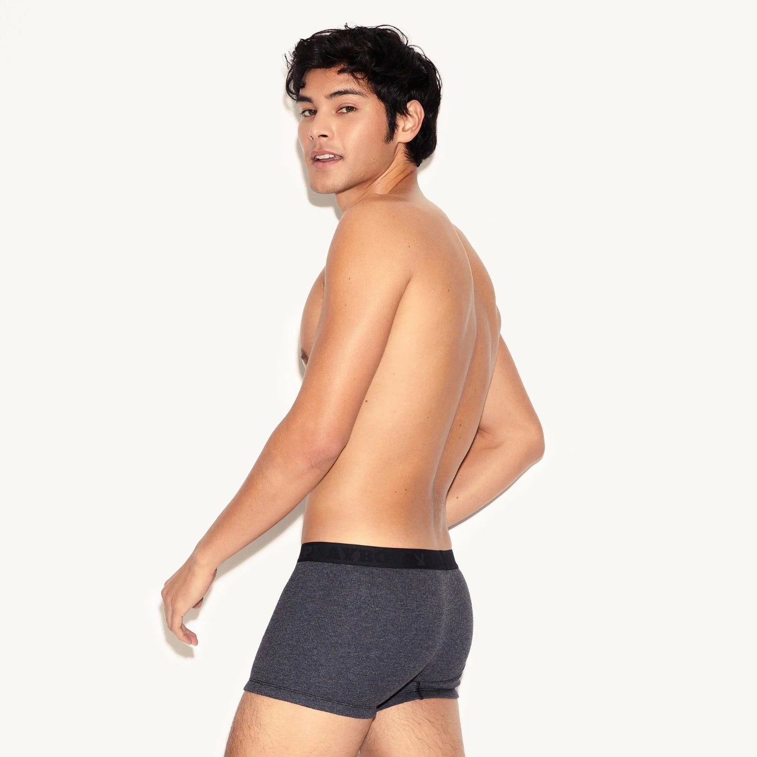 Shirtless man modeling dark grey ribbed men's trunk underwear against a plain background.
