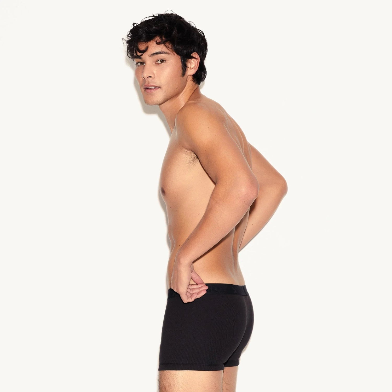 Shirtless man modeling black ribbed men's trunk underwear against a plain background