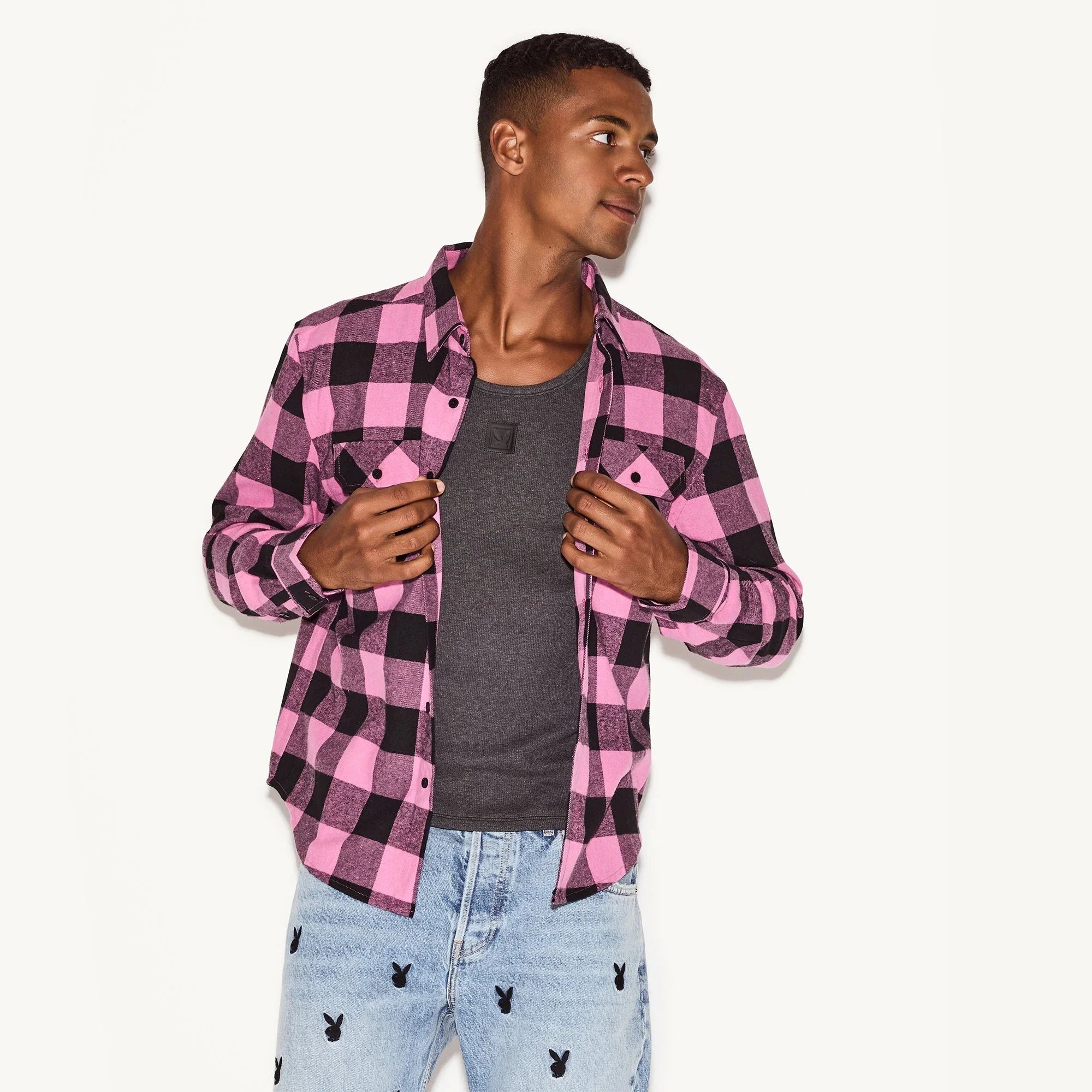 Man wearing a pink and black flannel long sleeve shirt over a gray t-shirt and light wash jeans with small black bunny graphics.