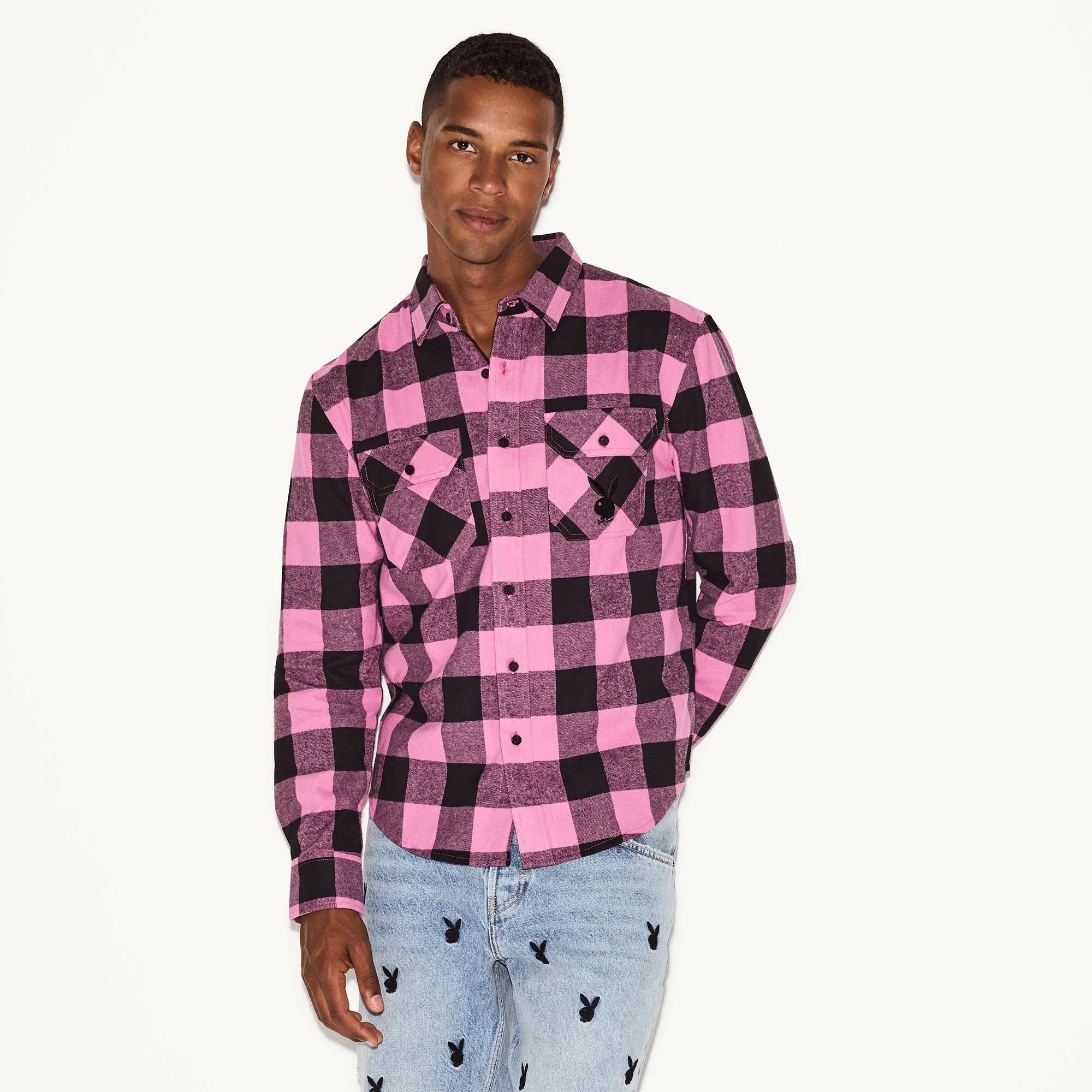 Man wearing pink and black plaid flannel shirt and light blue jeans with black bunny logos