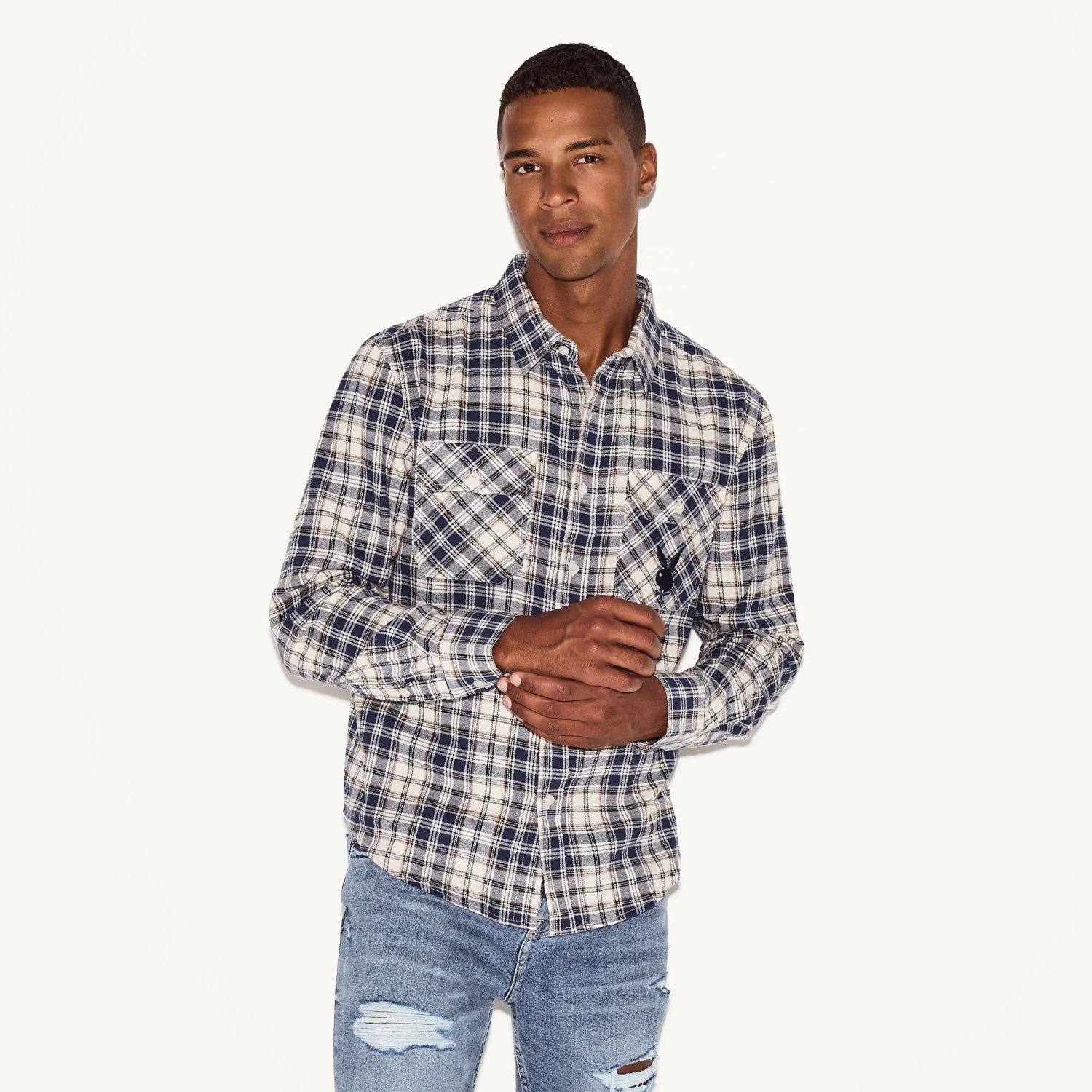 Man wearing blue and white plaid flannel long sleeve shirt with chest pockets and ripped jeans